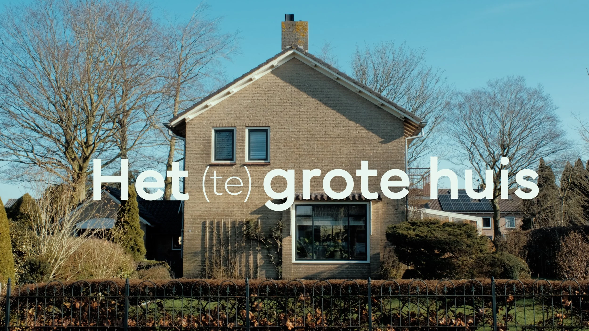 Een huis met een tuin en een hek, zonder mensen, onder een heldere blauwe lucht.