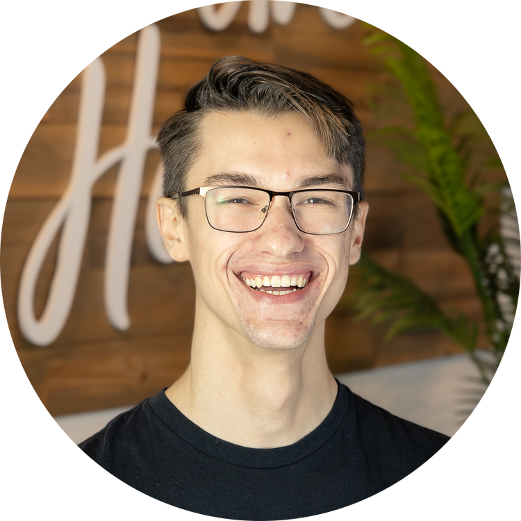 A young man with glasses smiling while looking at a phone or device.