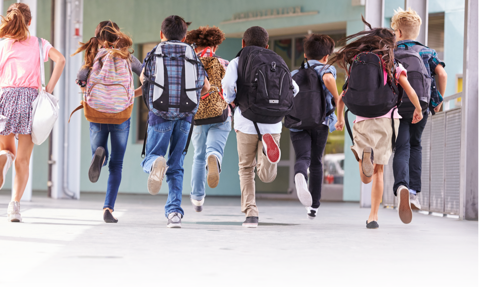 Group of children walking with backpacks outdoors, heading towards a building, possibly a school.