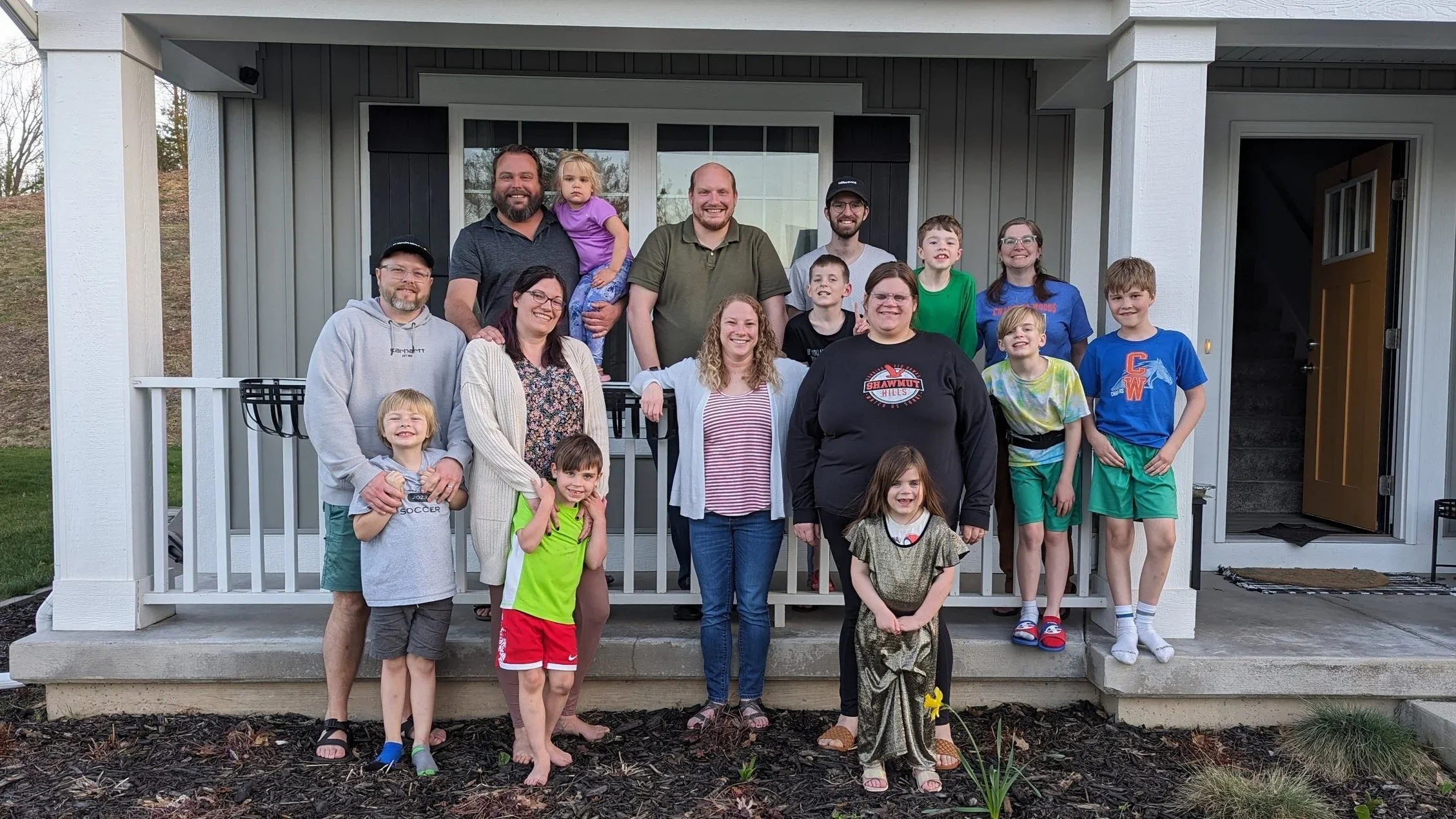 Group photo of adults and children standing on the front porch of a house, smiling and posing for the camera.