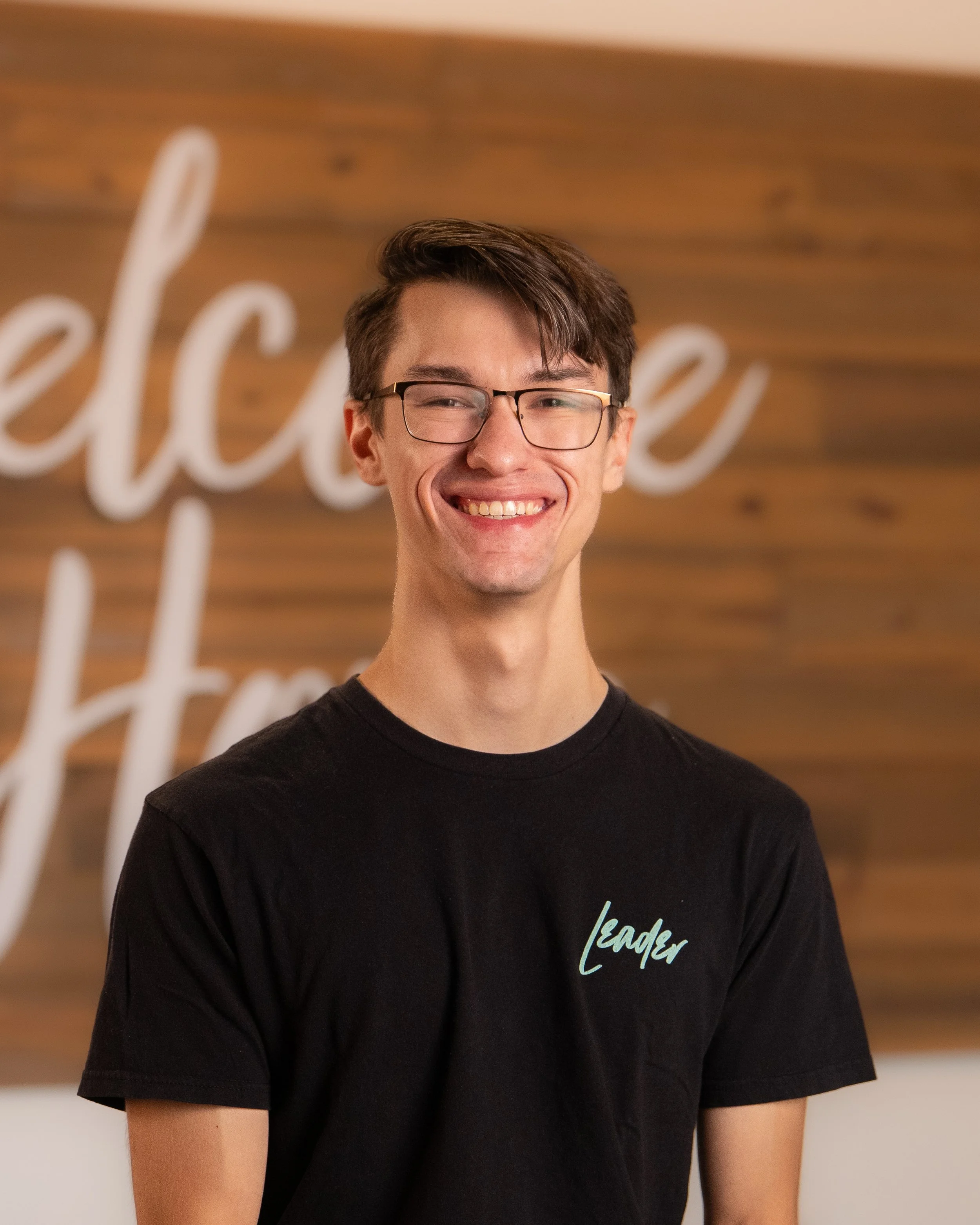 A young man with glasses smiling while looking at a phone or device.