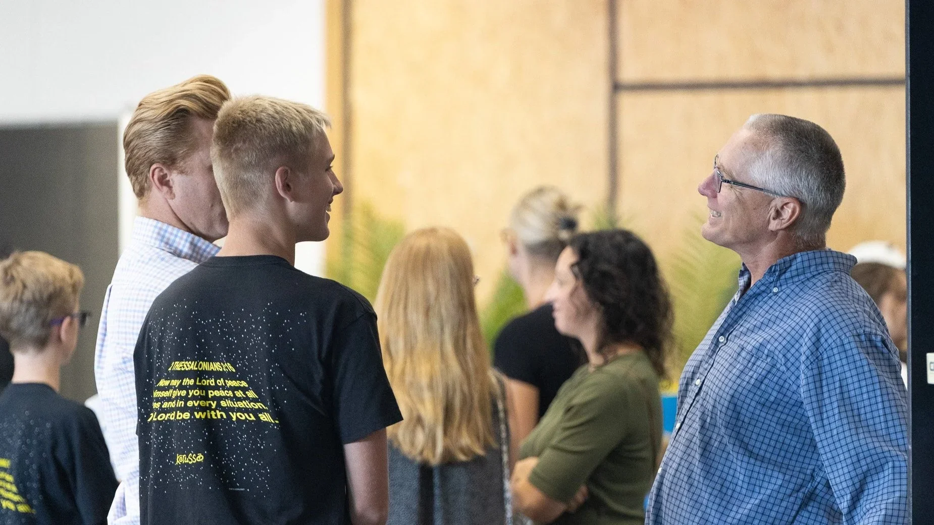 A group of people, including a young man and an older man, engaged in conversation at an indoor event.