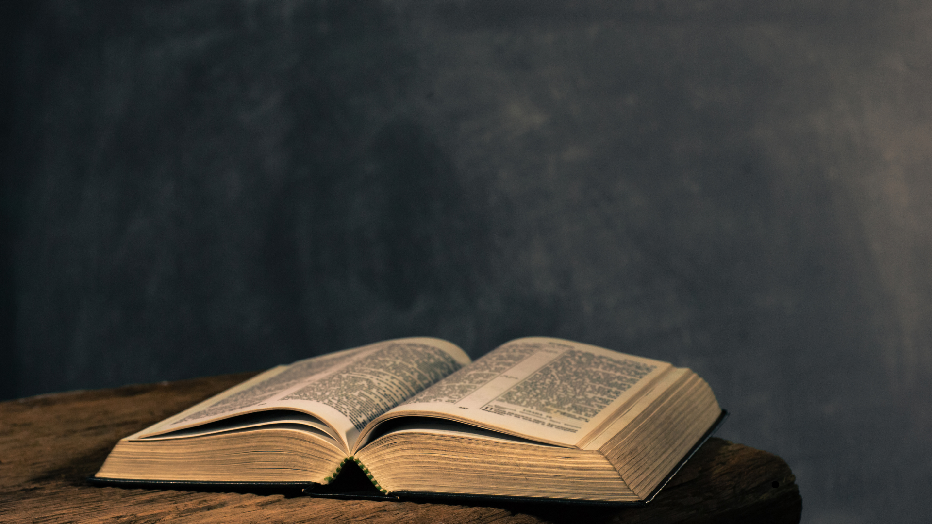 Open book with small print on a wooden surface against a dark gray background.