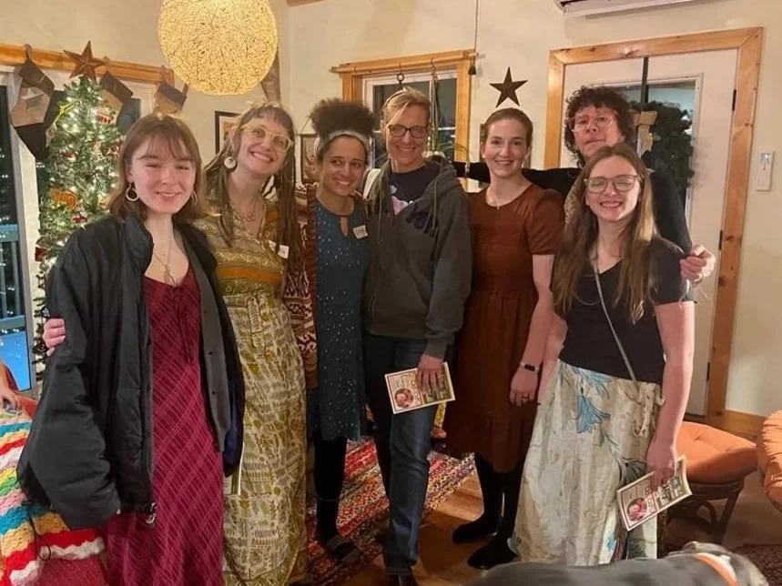 Six women standing together in a cozy, decorated living room, smiling for the photo.
