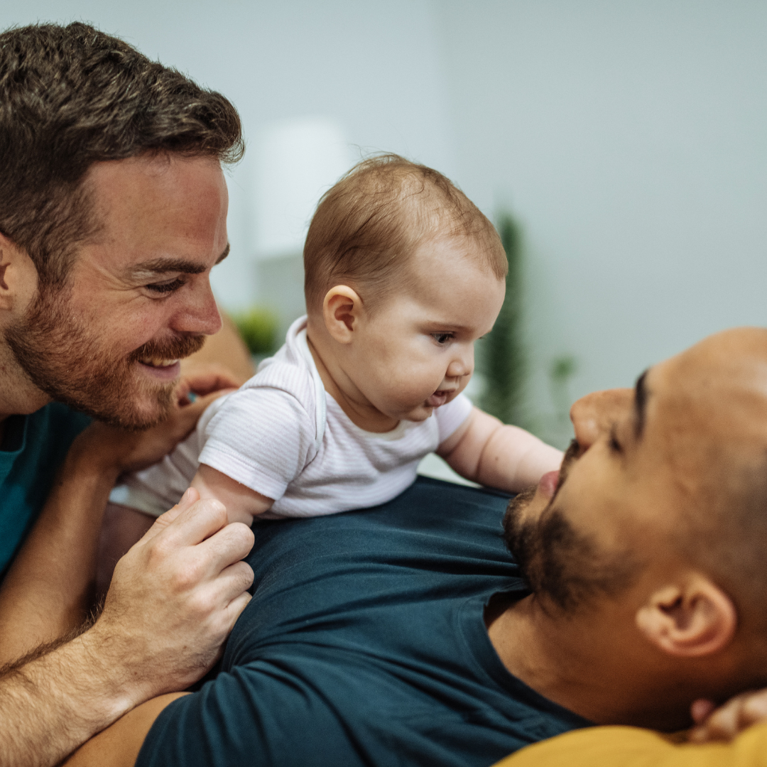 A happy family moment showing a toddler, a man, and a woman playing together on a bed.