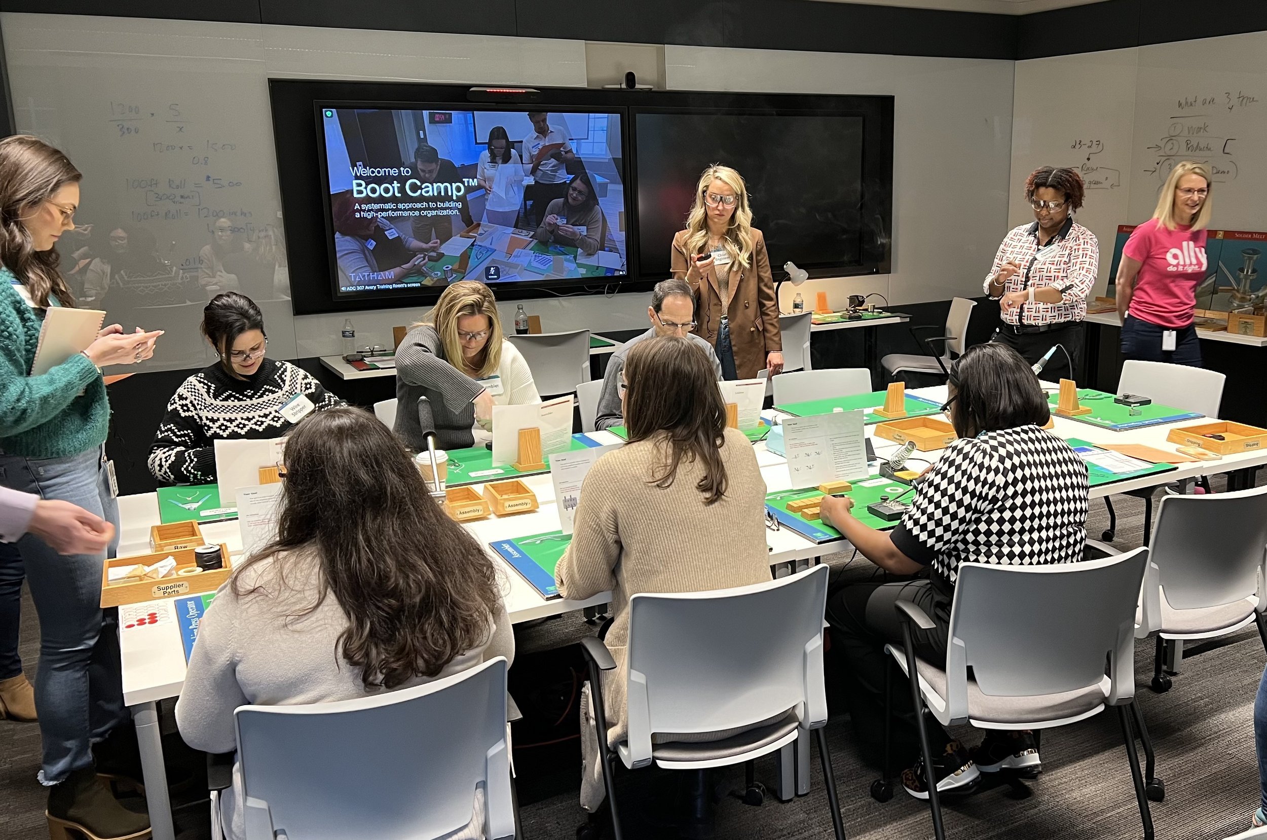 Group of people participating in a boot camp workshop in a conference room, with tables, monitors, and educational materials.