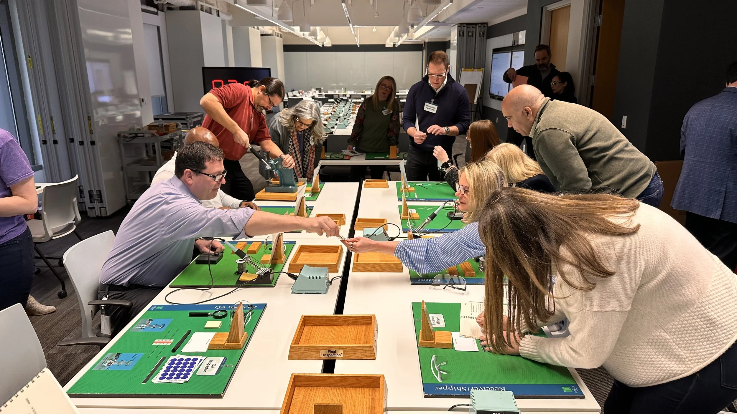 Group of people gathered around tables playing a game of Connect Four with large wooden pieces in a conference room.