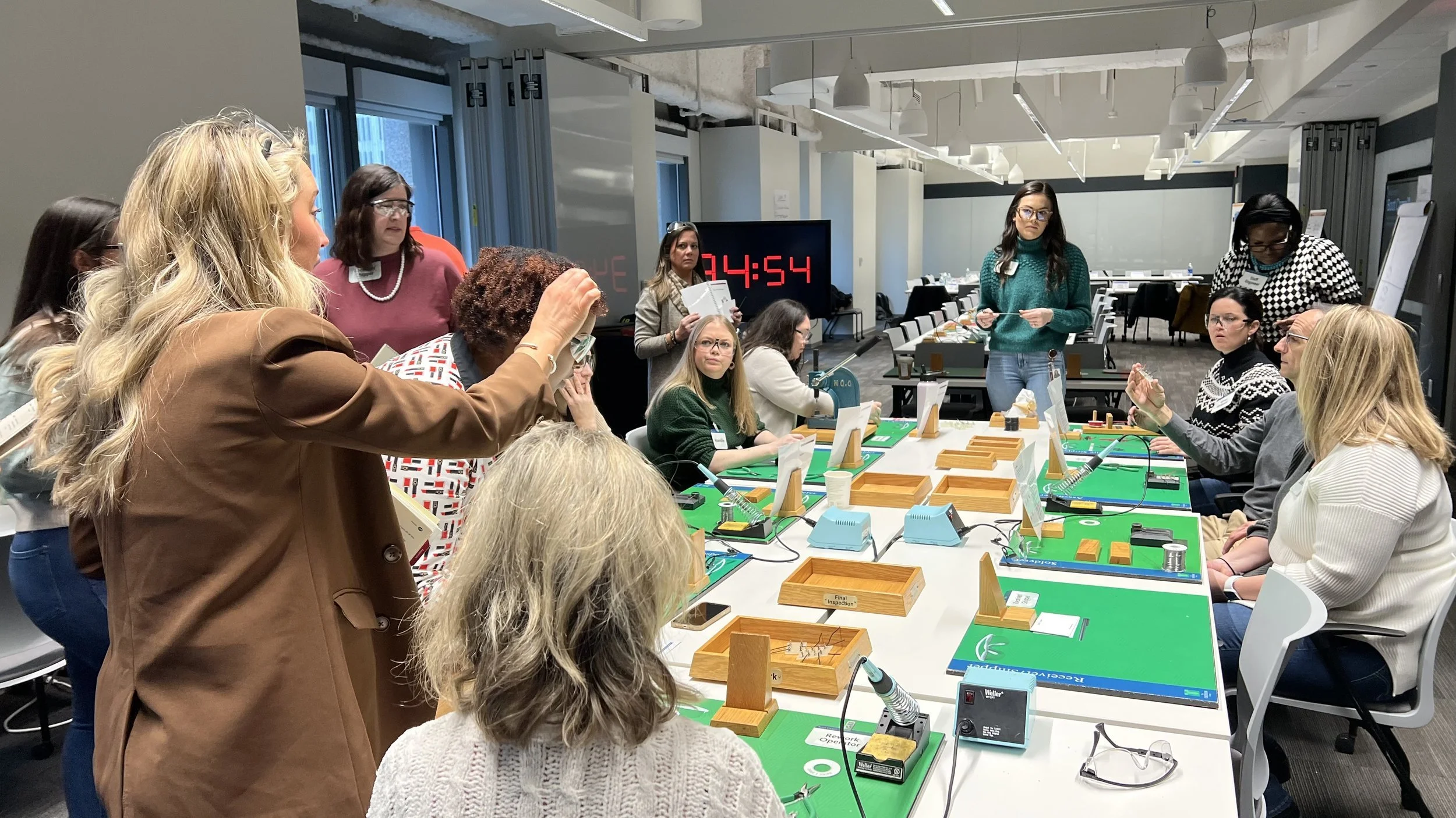 Group of women engaged in a tabletop game or demonstration in a conference room with digital timer and various small equipment.
