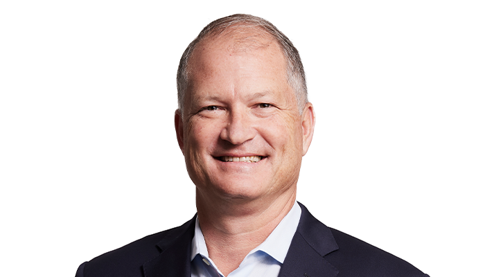 Portrait of a smiling man in a business suit with a white shirt, against a plain white background.