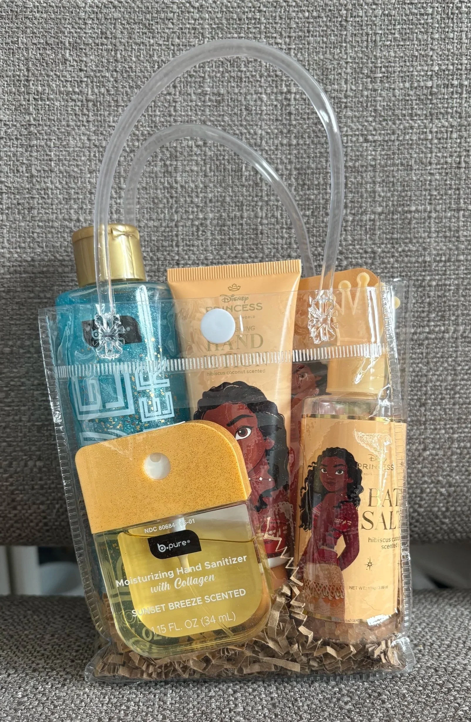 A Moana themed gift bag with hand sanitizer and lotion, bath salts, shower gel, 'Disney Princess Bath Sale.' The bag is on a gray textured surface.