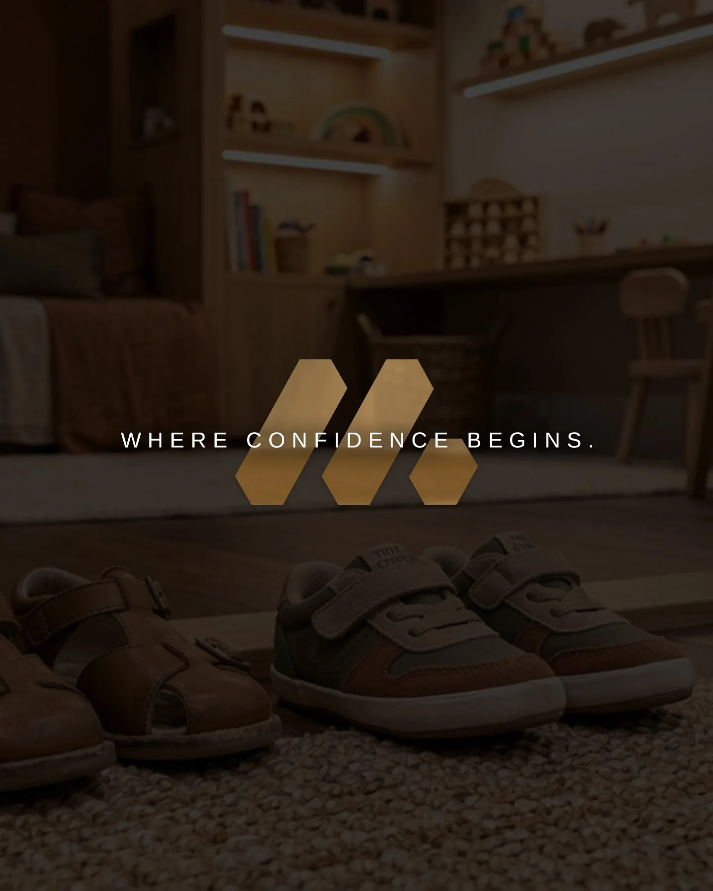 A pair of children's shoes, one brown and one with a tan and green design, placed on a carpeted floor. In the background, a cozy living room with a sofa, bookshelves, and a desk is visible. Text overlay says "Where confidence begins."