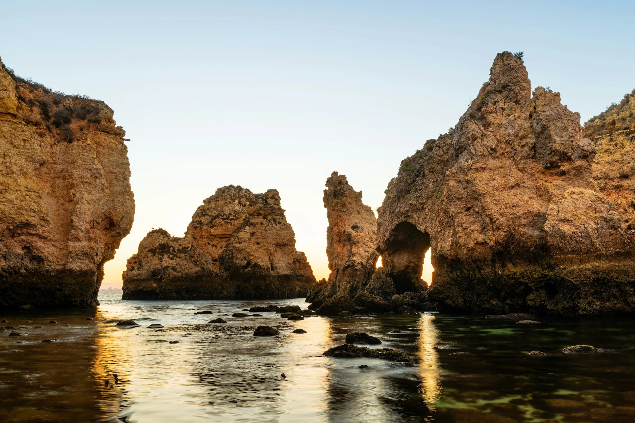 Rock formations on the coast at sunset with the ocean and sky in the background.