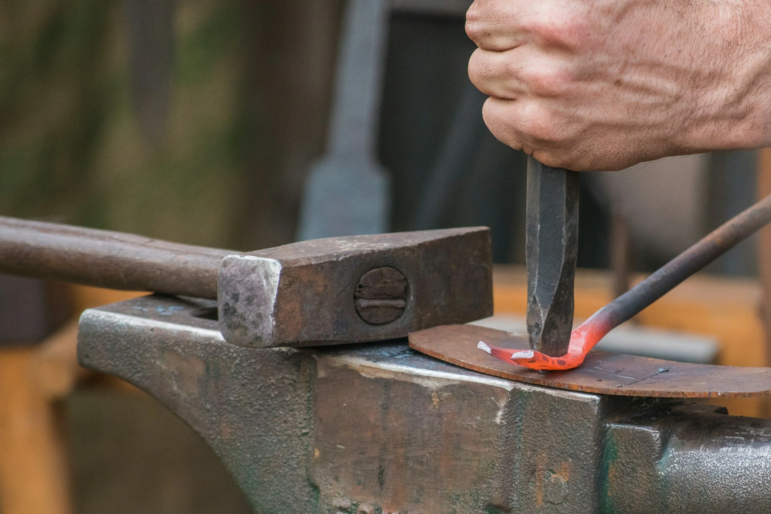 A person working on a metal project, using tools on a metal piece clamped to a workbench.