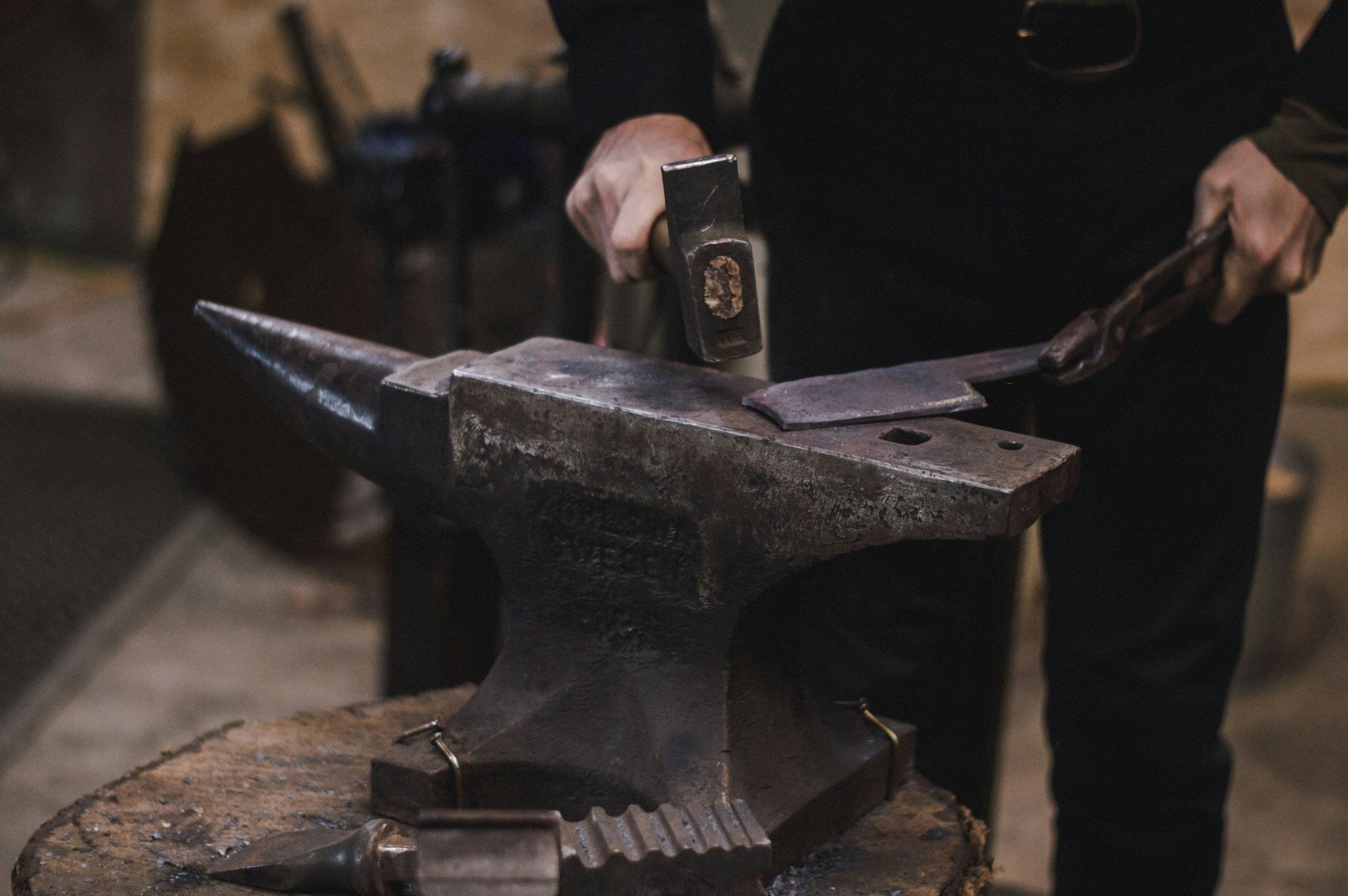 Blacksmith forging metal using a hammer and anvil in a workshop.