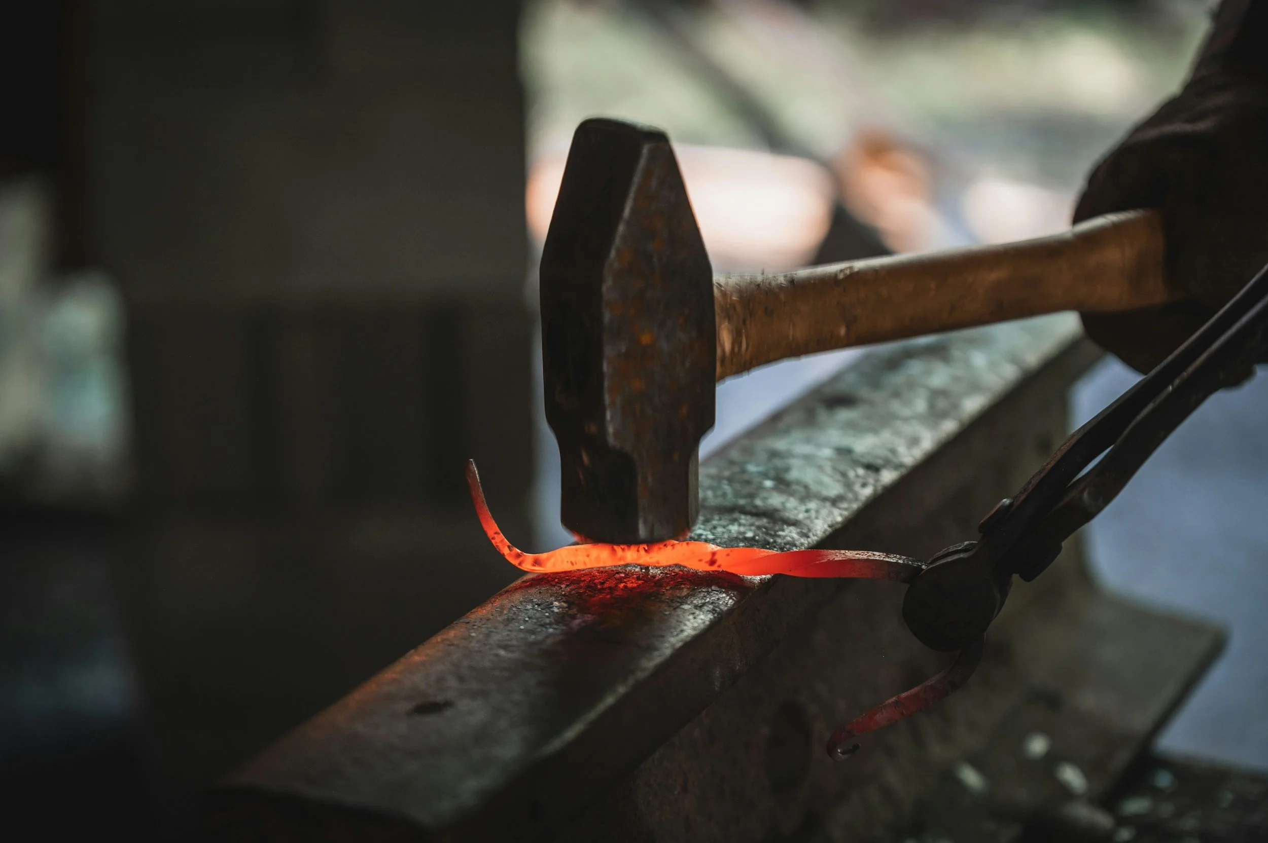 A blacksmith hammering a glowing piece of red-hot metal on an anvil in a workshop.