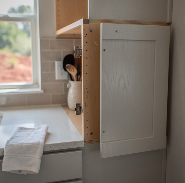 A white cabinet door on a wooden frame sits on a countertop near a window with a cloth beneath it.