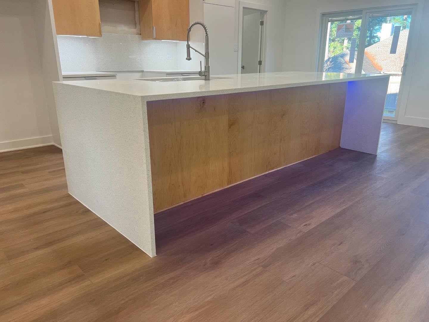 Modern kitchen with a white and wood kitchen island, stainless steel sink with a tall faucet, and wood flooring. Large windows with a view of trees and neighborhood roofs.