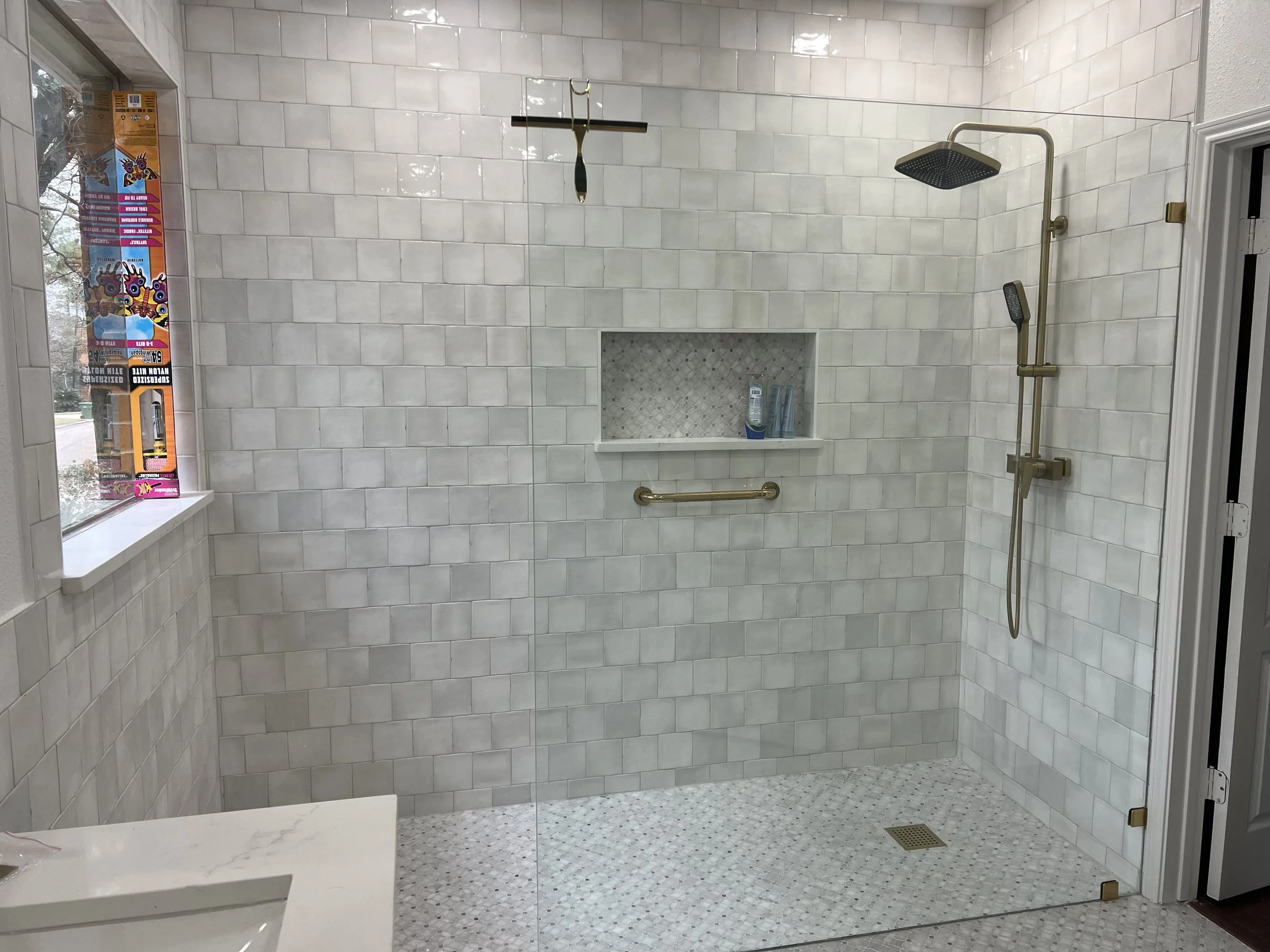 A modern walk-in shower with white subway tile walls, a ceiling-mounted rainfall showerhead, a handheld showerhead, and a built-in small niche for toiletries. There is a window on the left side and a window or door on the right side.