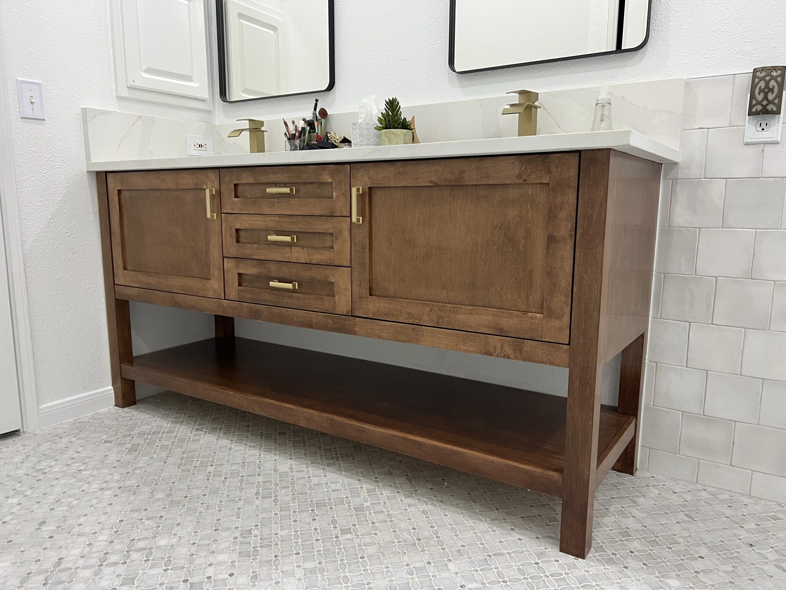 Bathroom vanity with a wooden cabinet, two sinks, mirrors, and various small items on the countertop.