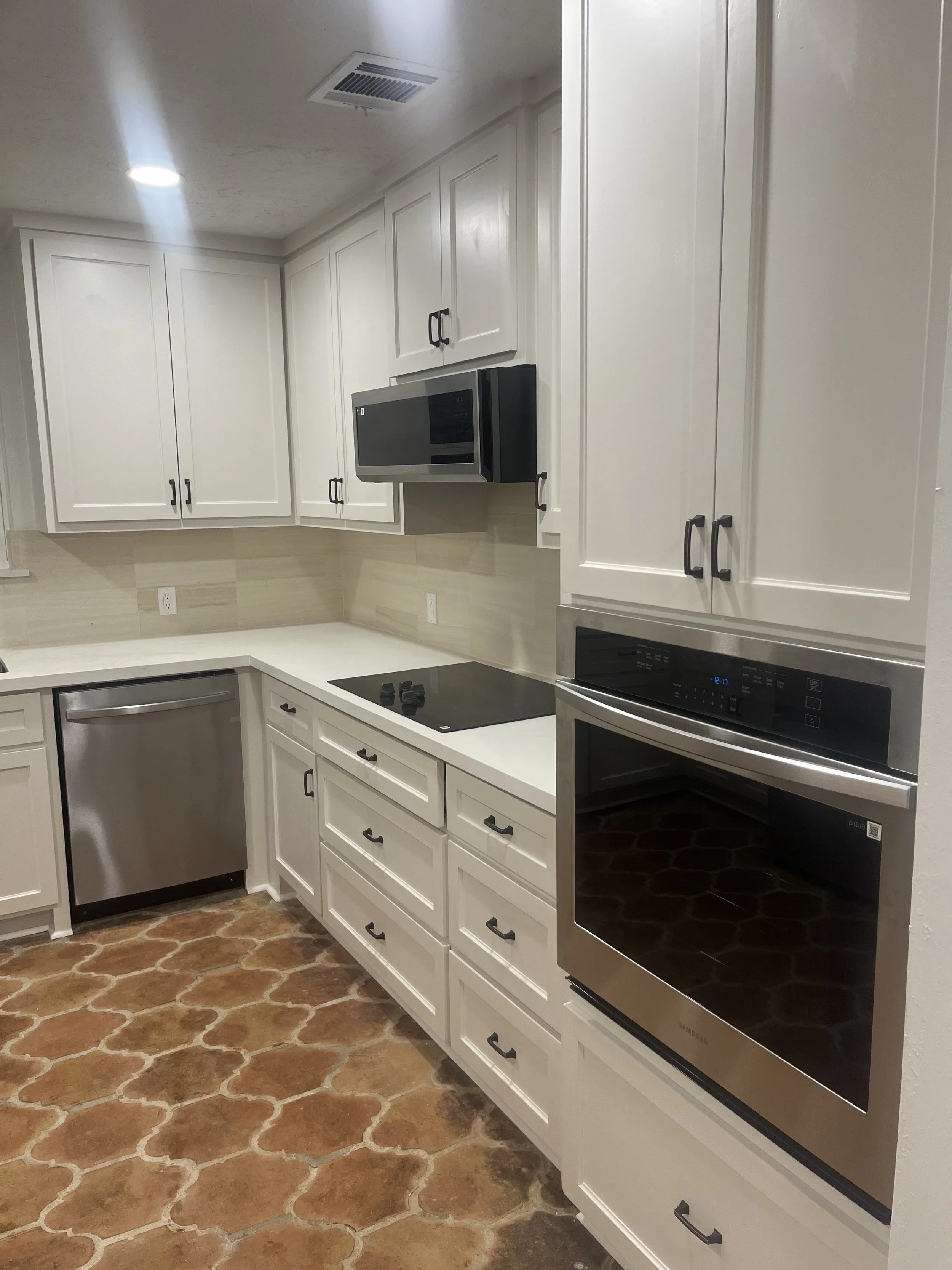 Kitchen with white cabinets, built-in microwave, electric stovetop, and oven, with terracotta tile flooring.