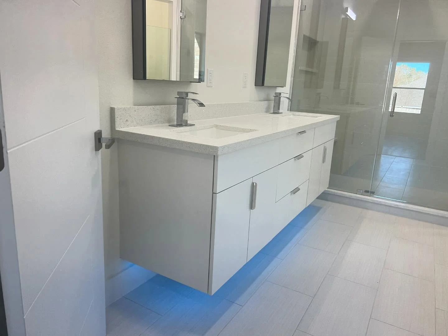 Modern bathroom with double sink vanity, mirrors, and glass shower enclosure.