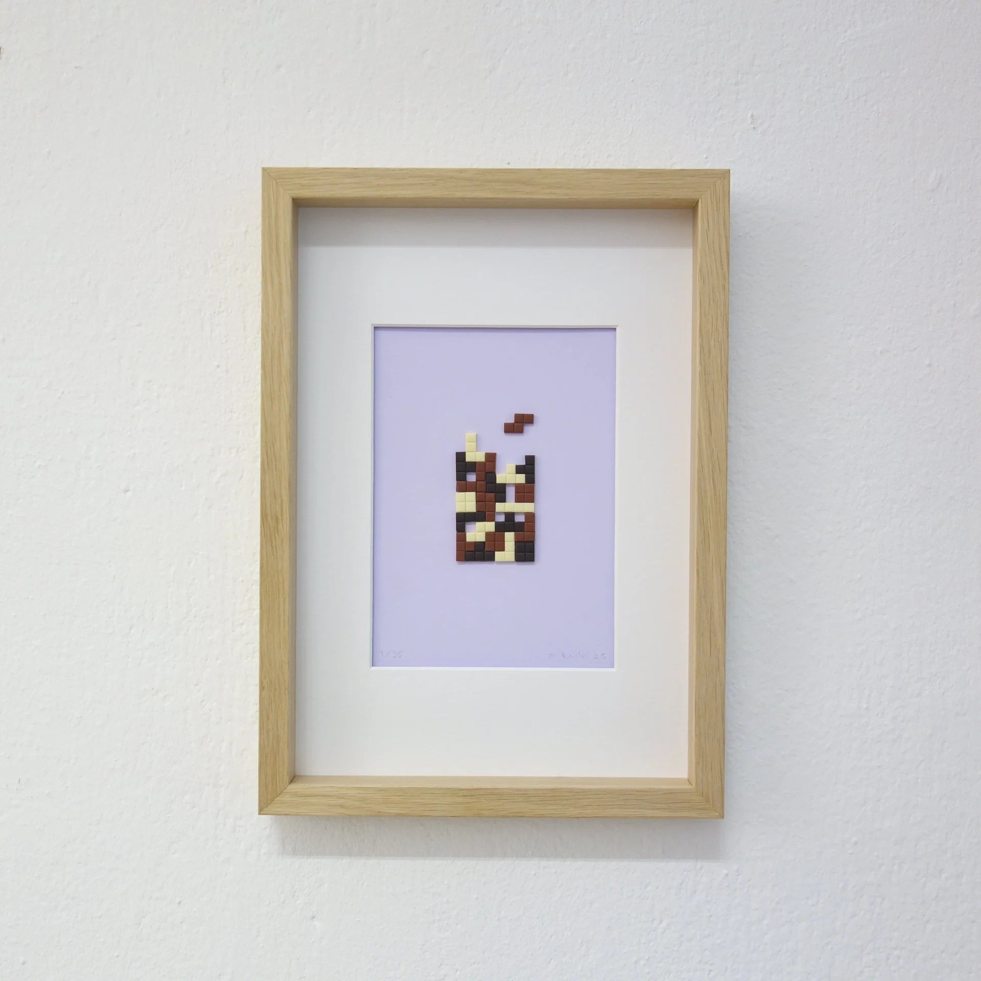 Kunstwerk mit pixelartähnlichem Bild eines Tieres, in einem Holzbilderrahmen, an einer weißen Wand.