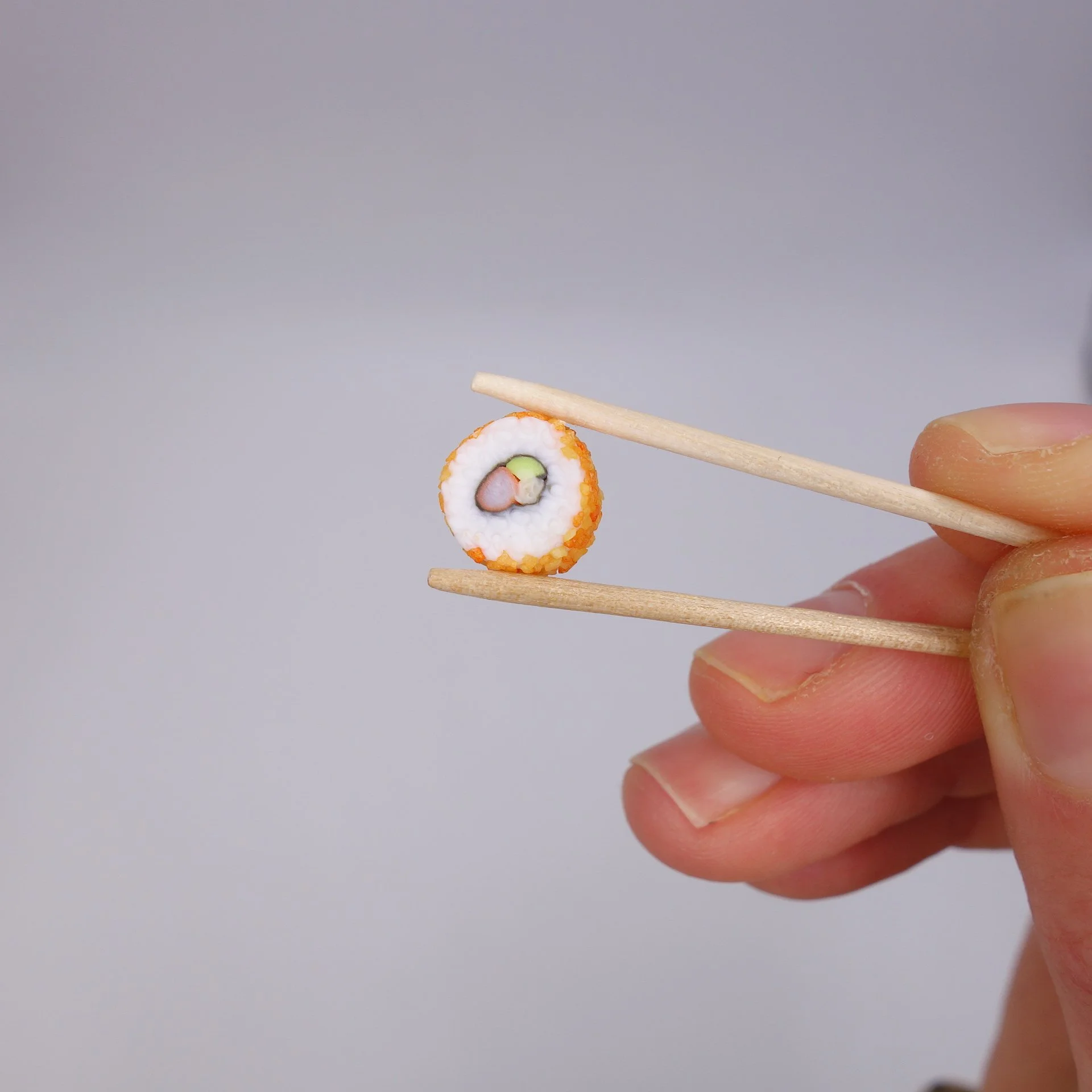 Nahaufnahme von Sushi, das mit Essstäbchen gehalten wird, vor einem neutralen grau Hintergrund.