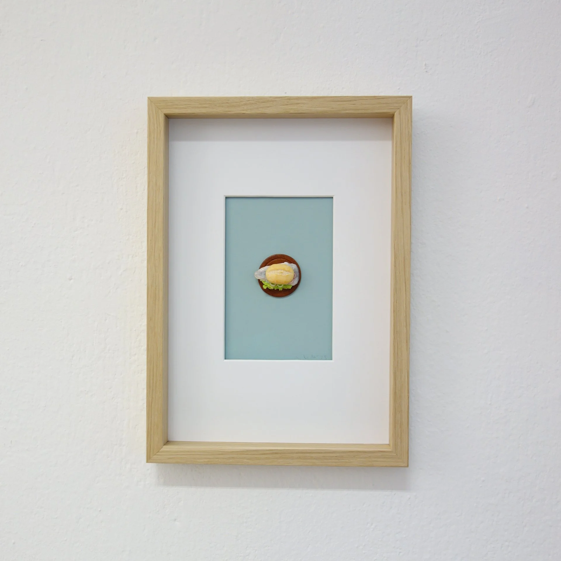 Leinwand mit einem Miniatur-Burger, an einer Wand in einem Holzrahmen aufgehängt.