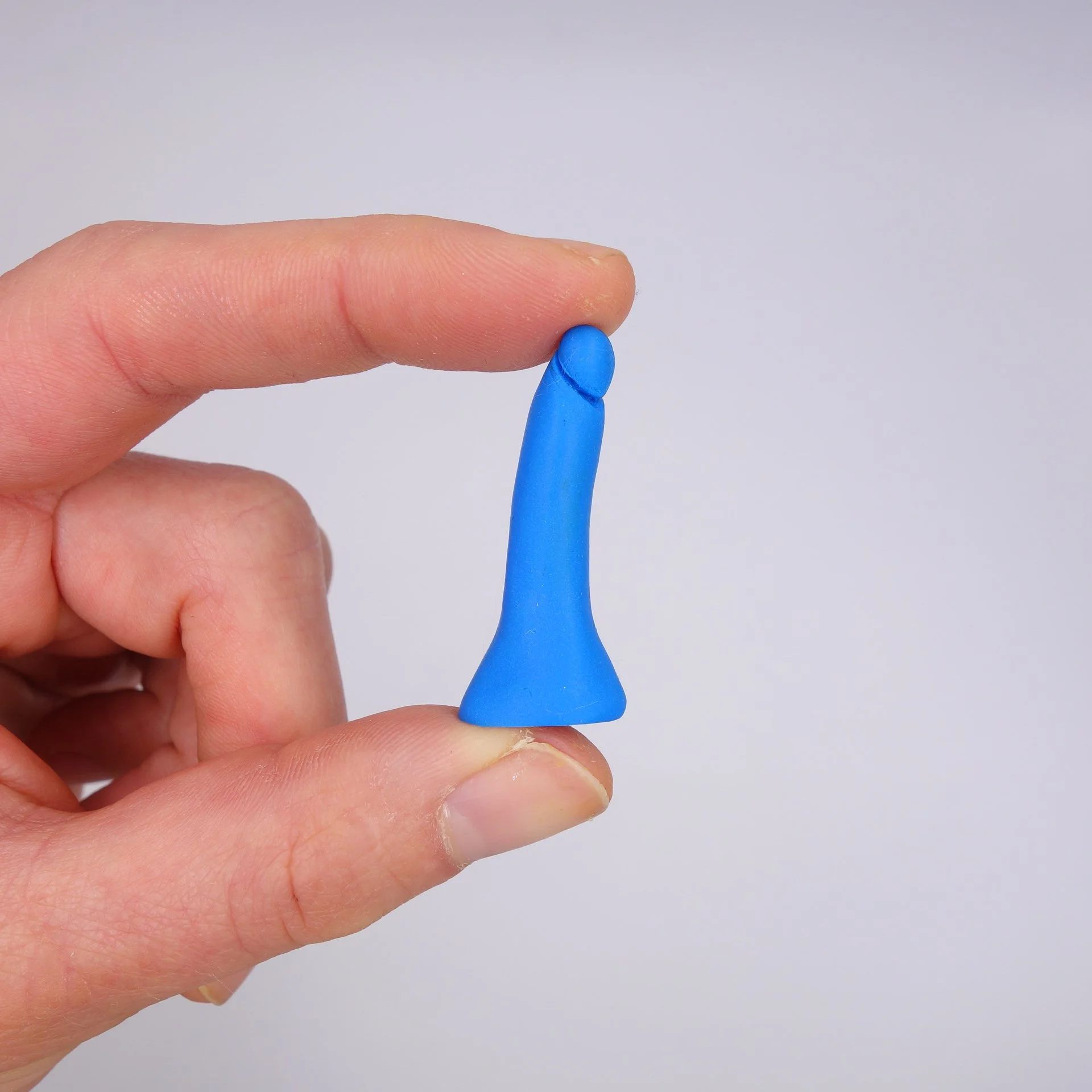 Hand hält ein bluefarbenes Teststäbchen zwischen Daumen und Zeigefinger gegen hellgrauen Hintergrund.