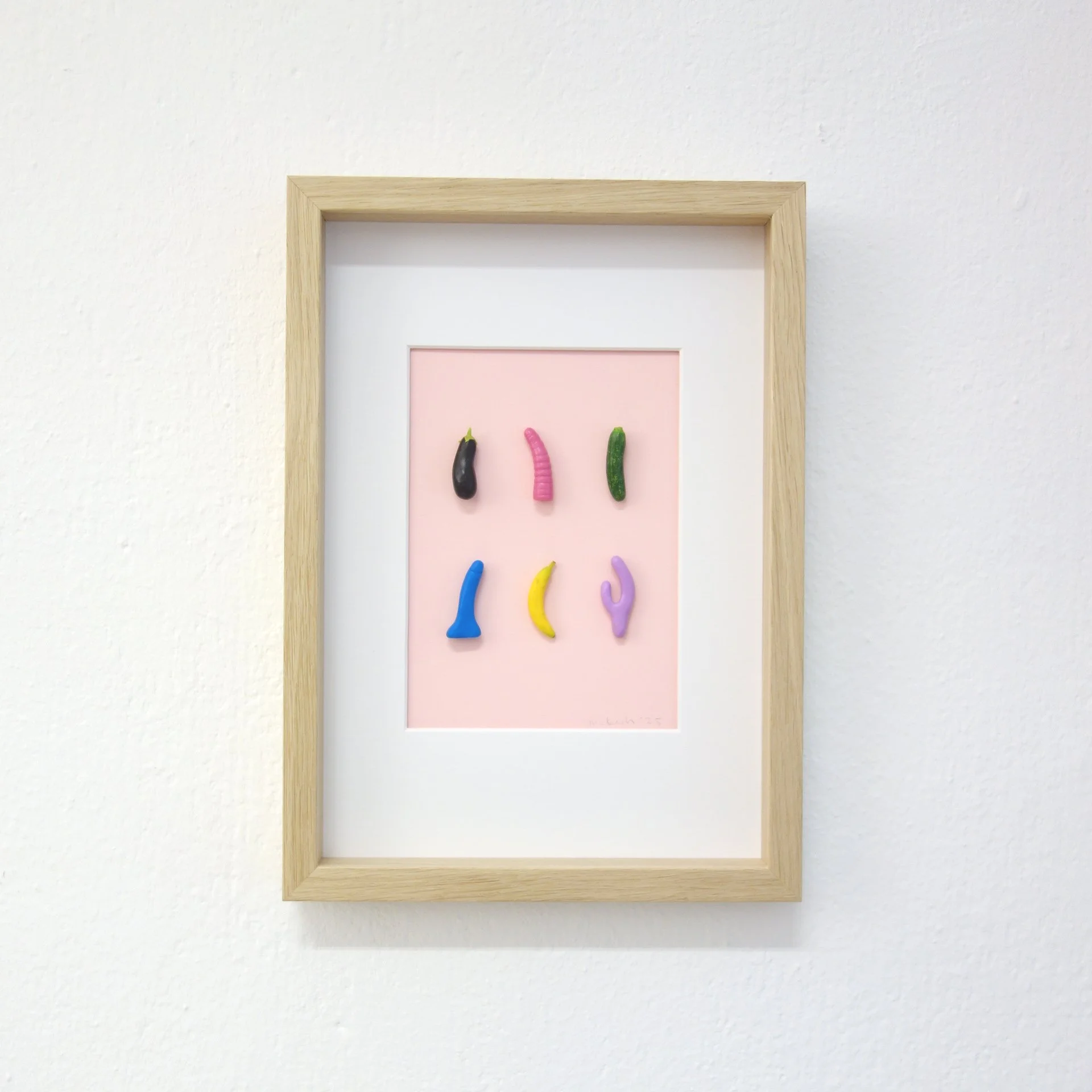 Kunstwerk mit mehreren bunten Gummiwürmern auf rosa Hintergrund in einem Holzrahmen