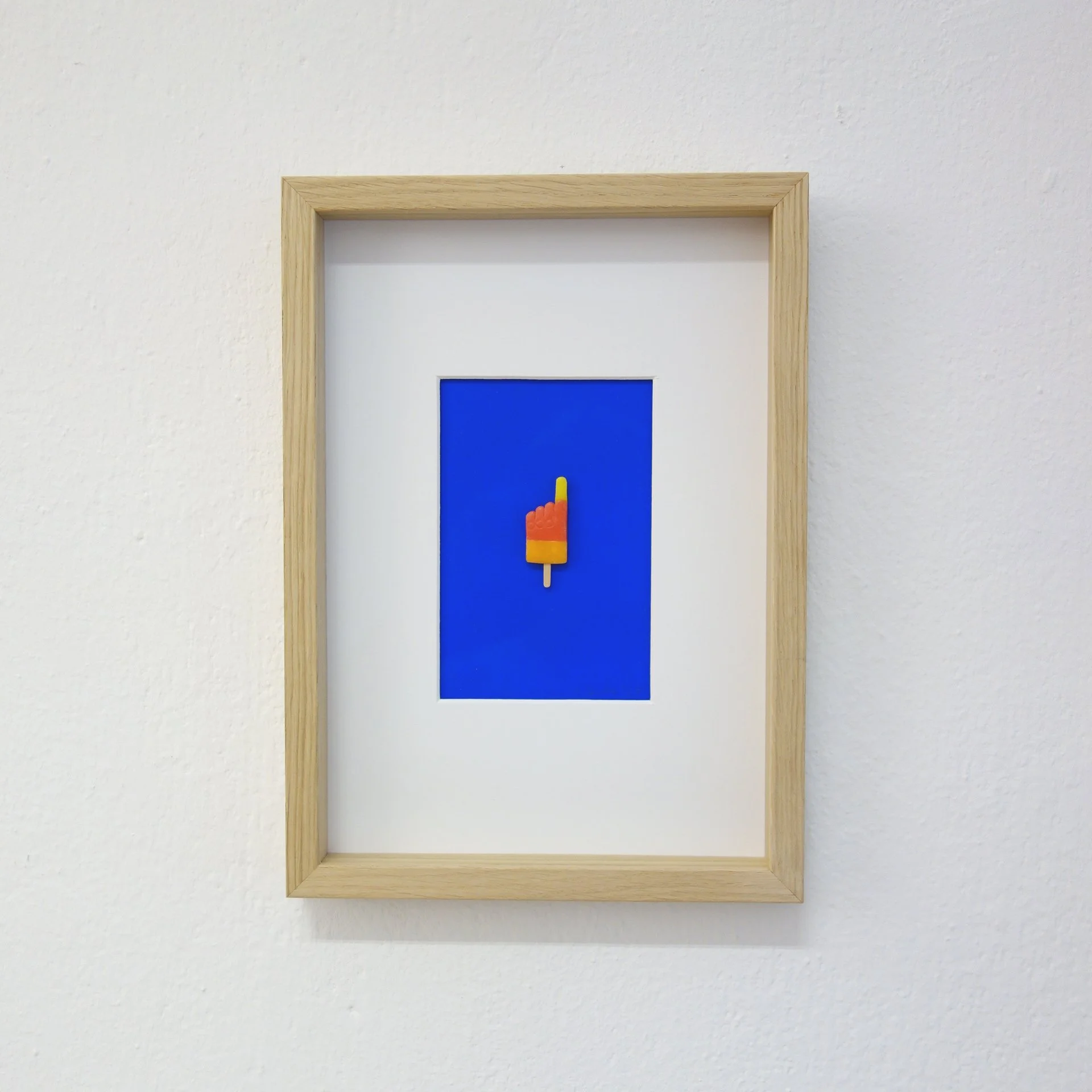 Kunstwerk mit einem blauen Hintergrund und einem mehrfarbigen Popsicle in der Mitte, eingerahmt in Holz