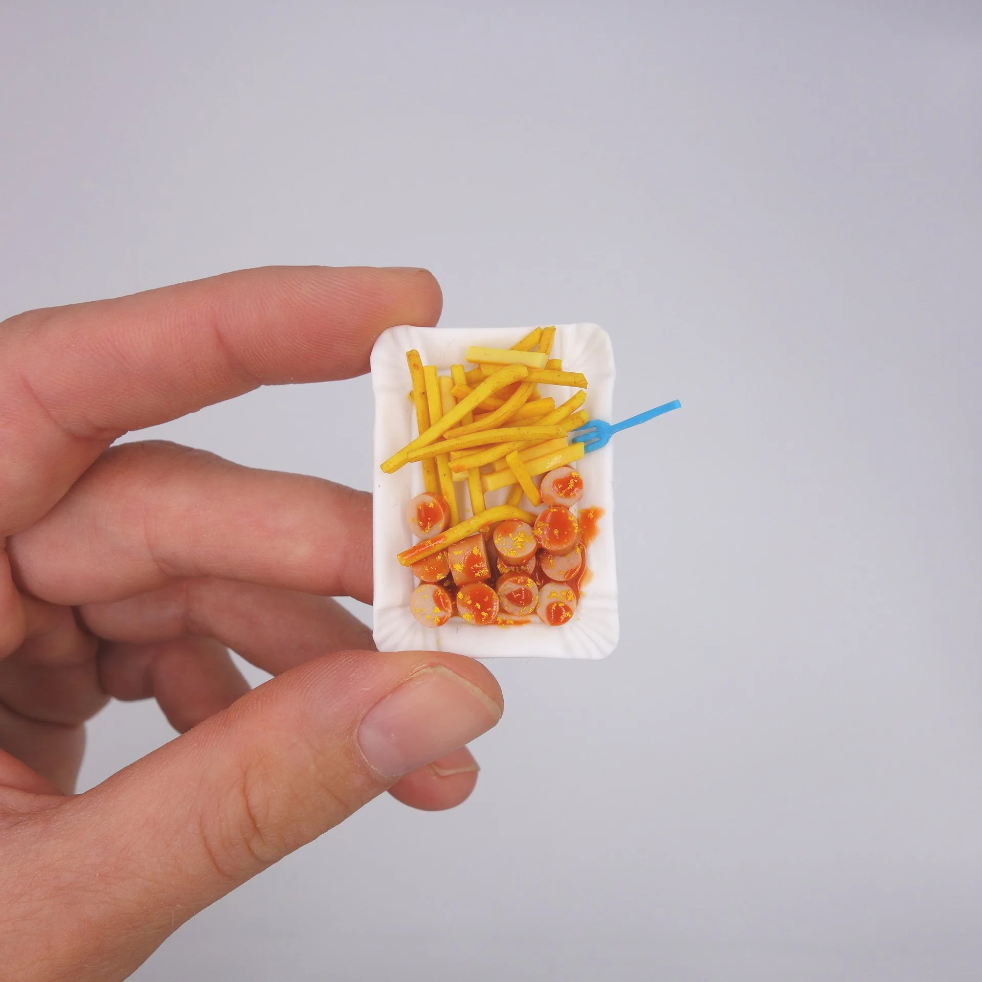 Hand hält eine kleine weiße Schale mit französischen Pommes und kleinen Tomaten.