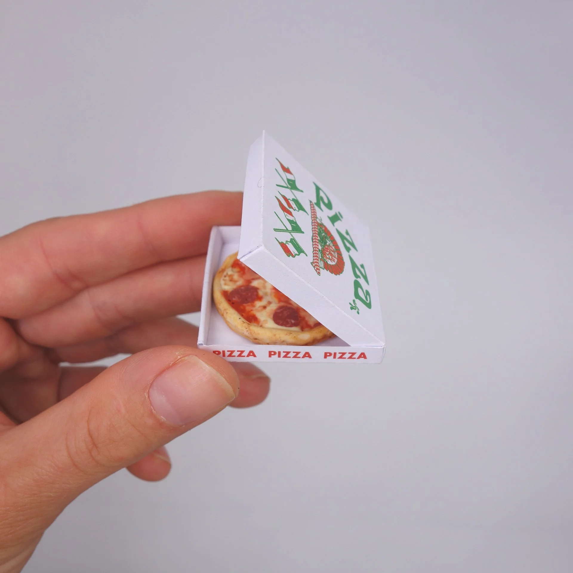 Hand hält eine Miniaturpizza in einer Pizza-Box.
