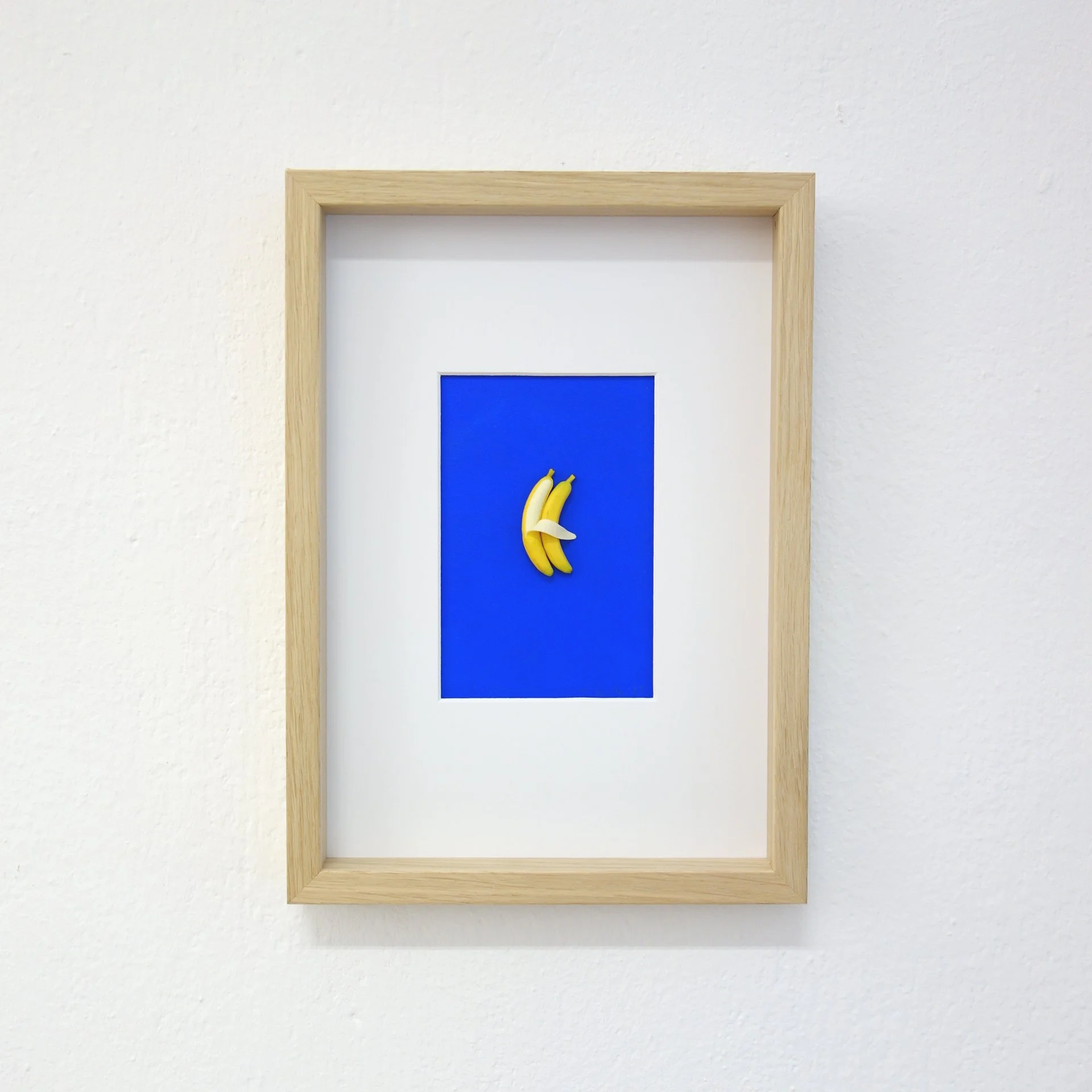 Fotografie eines Bilderrahmens an einer weißen Wand, mit einem blauen Hintergrund und einer abgebildeten Bananen-Darstellung.