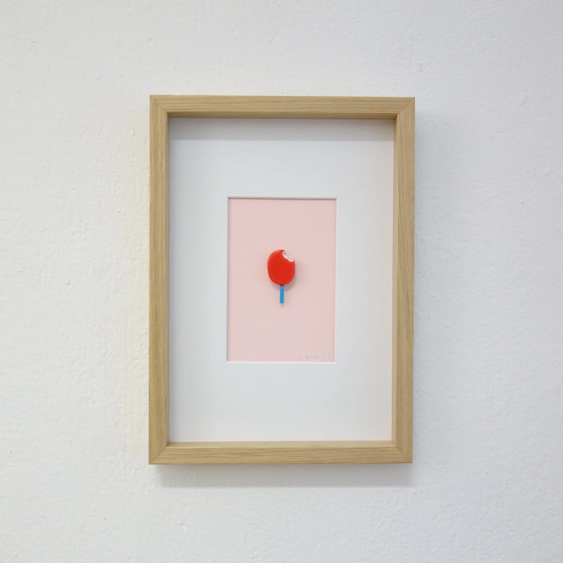 Nahaufnahme eines Bilderrahmens an einer weißen Wand mit einem pinken Hintergrund und einem roten Gegenstand in der Mitte.