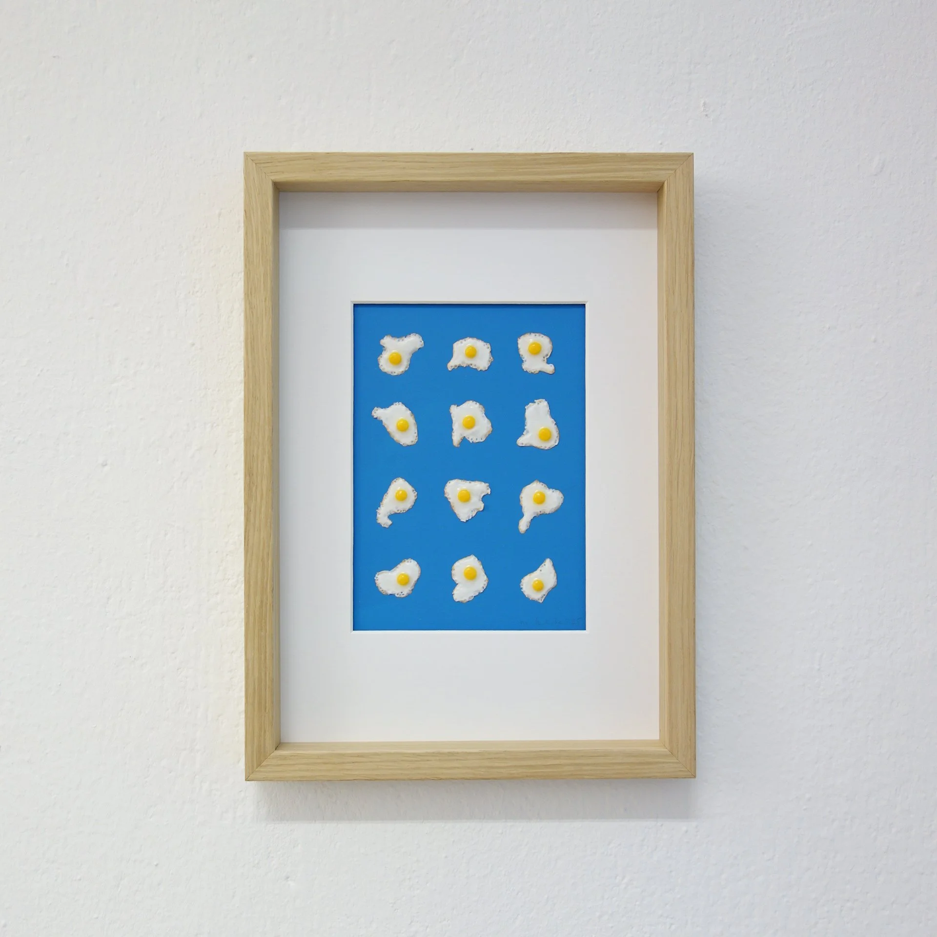 Gerahmtes Kunstwerk mit kleinen Eiern auf blauem Hintergrund