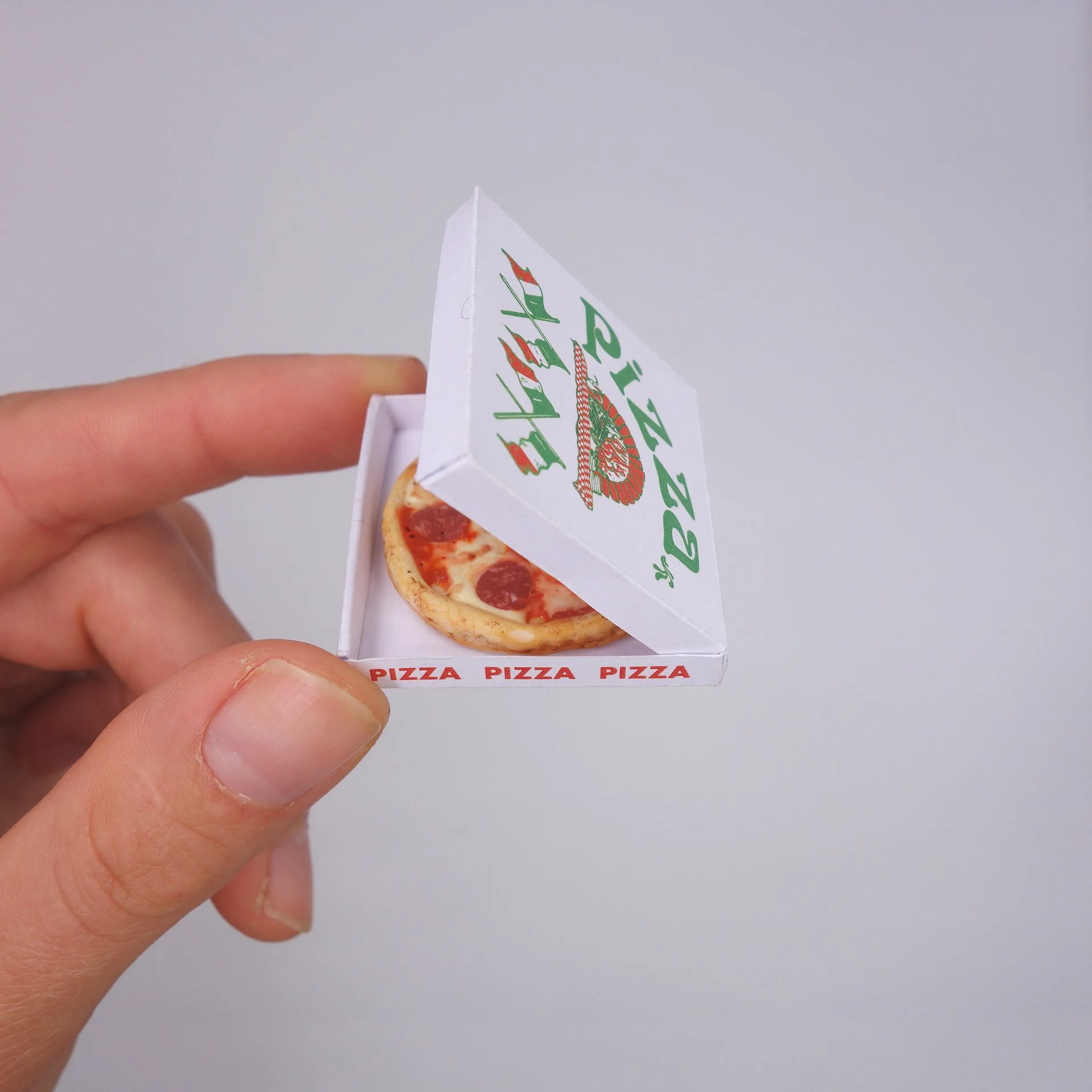Hand hält eine Mini-Pizza in einer Pizzabox, auf der sich das Wort 'Pizza' wiederholt.
