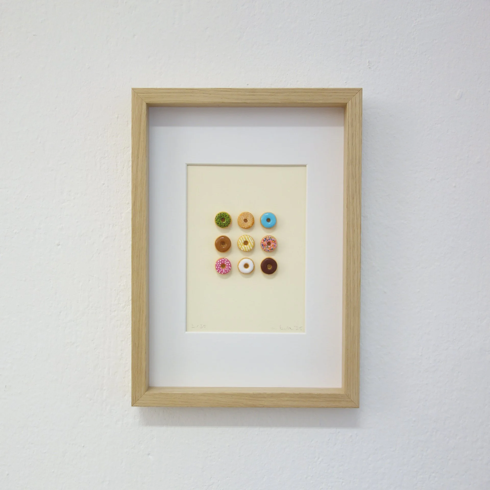 Ein Bilderrahmen mit kleinen bunten Donuts als Dekoration, hängt an einer weißen Wand.
