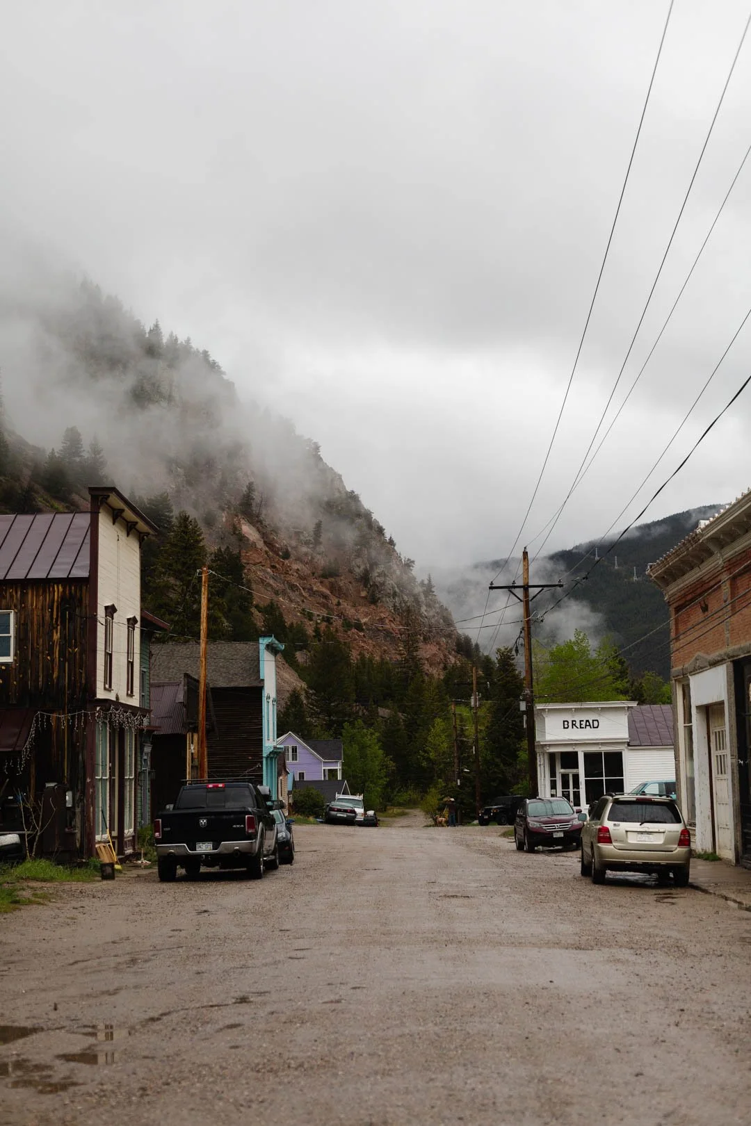 A small town surrounded by trees and old buildings, set against a mountain with mist and clouds in Rocky, Mountains, Colorado