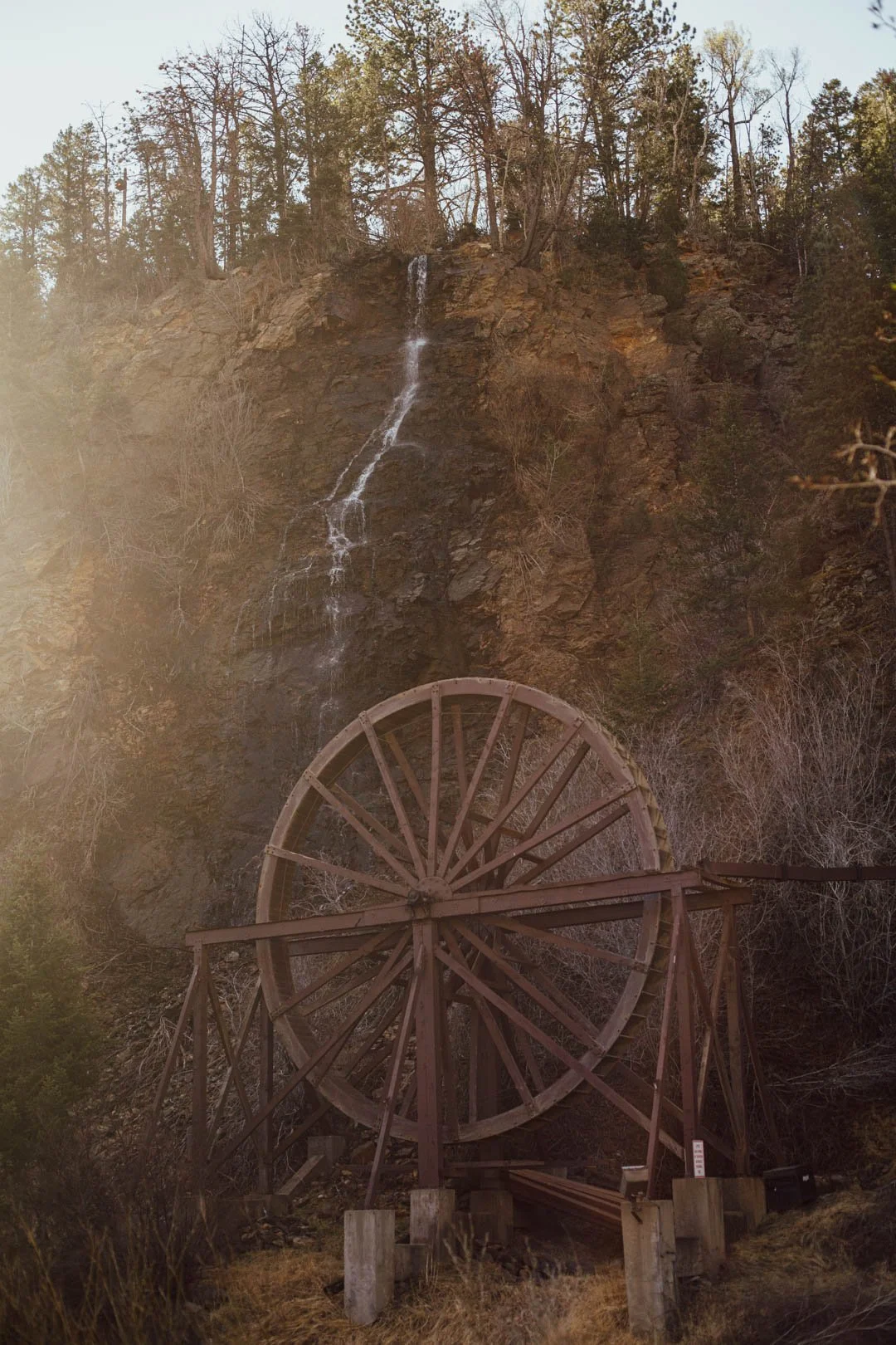 An old wooden water wheel located at the bottom of a rocky hill with a waterfall flowing down the mountain near Denver, Colorado in the Rocky Mountains.