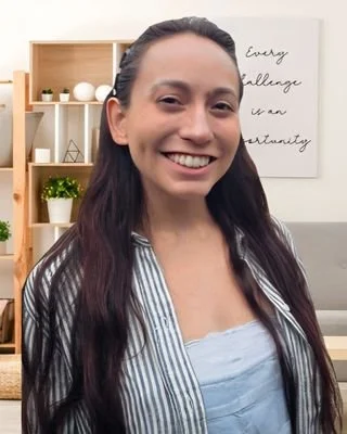A woman smiling in front of a bookshelf and a framed quote that reads 'Every challenge can be an opportunity'.
