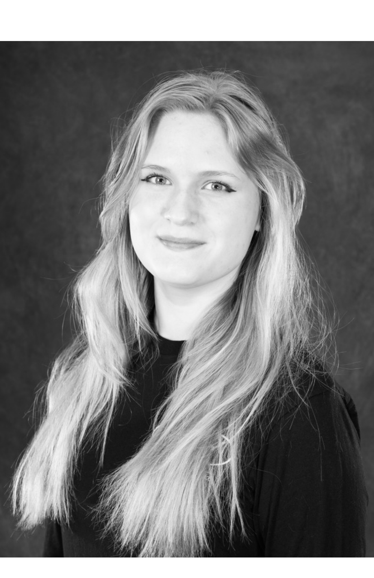 Black and white portrait of a woman with long wavy hair, wearing a dark top, with a neutral background.
