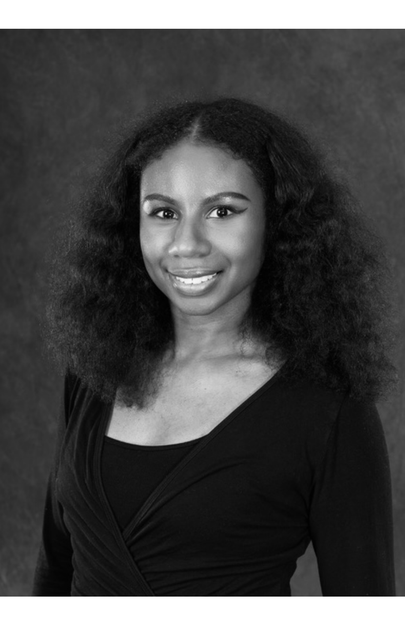Black and white portrait of a smiling woman with curly hair, wearing a dark top with a V-neck, against a textured background.