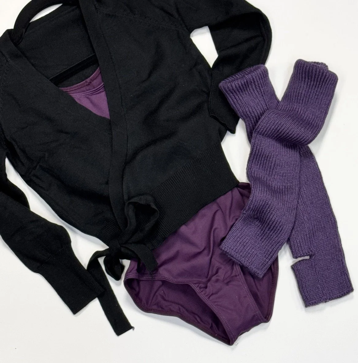 Black jacket, purple shirt, purple shorts, and purple knit gloves laid out on a white surface.