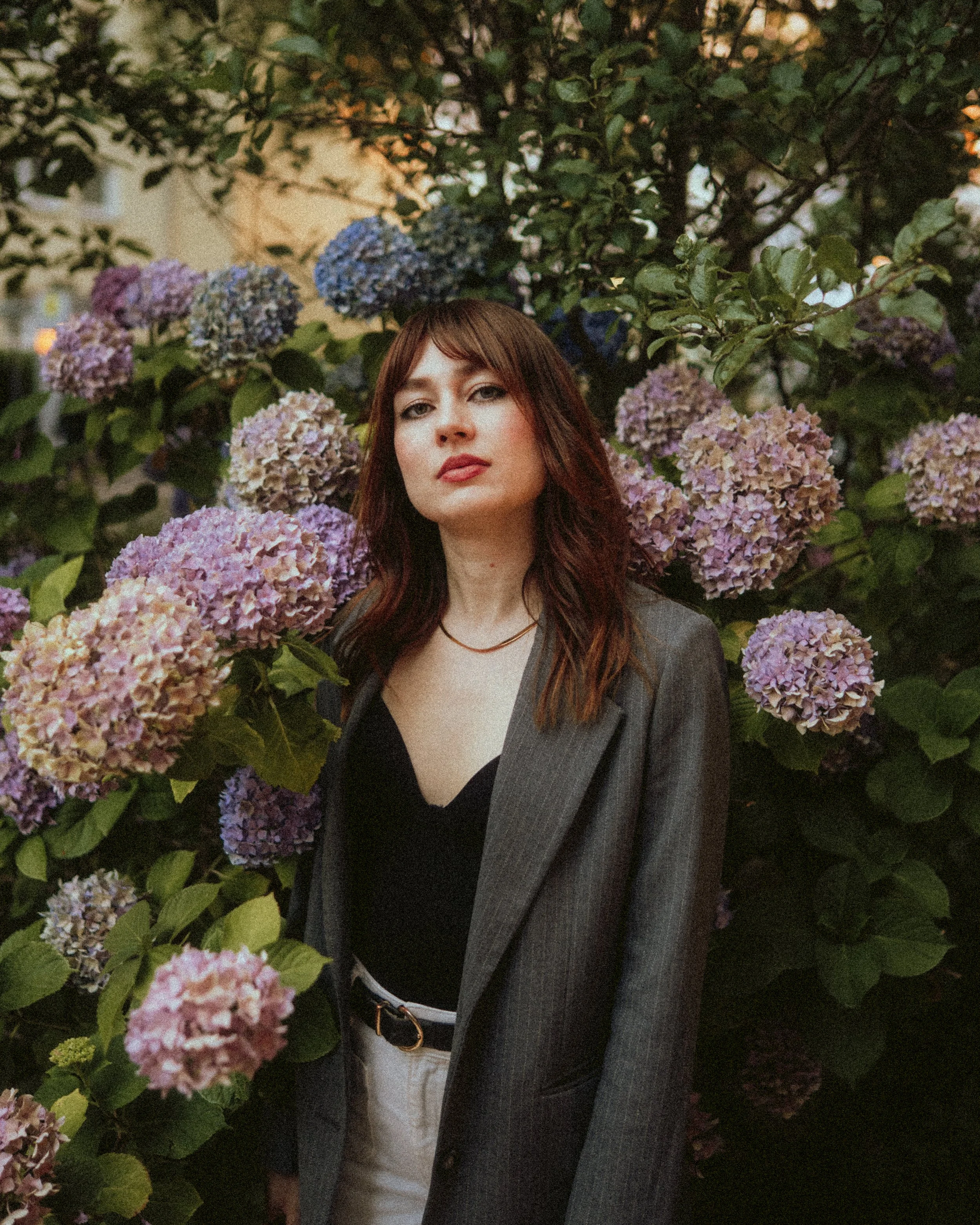 Portrait von einer Frau im Business-Outfit vor einem Busch mit Hortensienblumen in Dortmund.