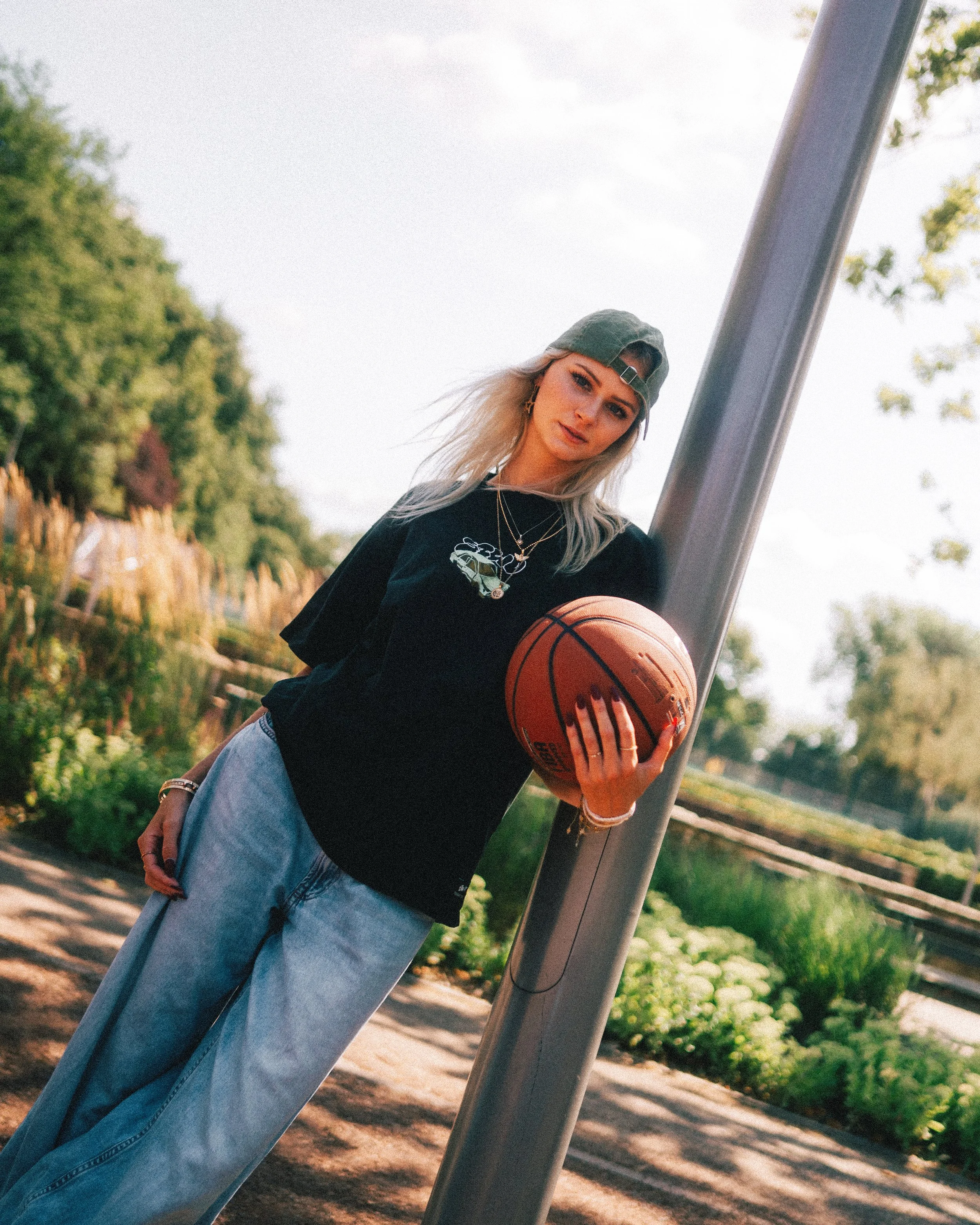 Portraitfotografie von einer Frau mit grünem Baseballcap und schwarzem T-Shirt, die einen Basketball hält und in Dortmund Nordstadt an einer Straßenlaterne steht