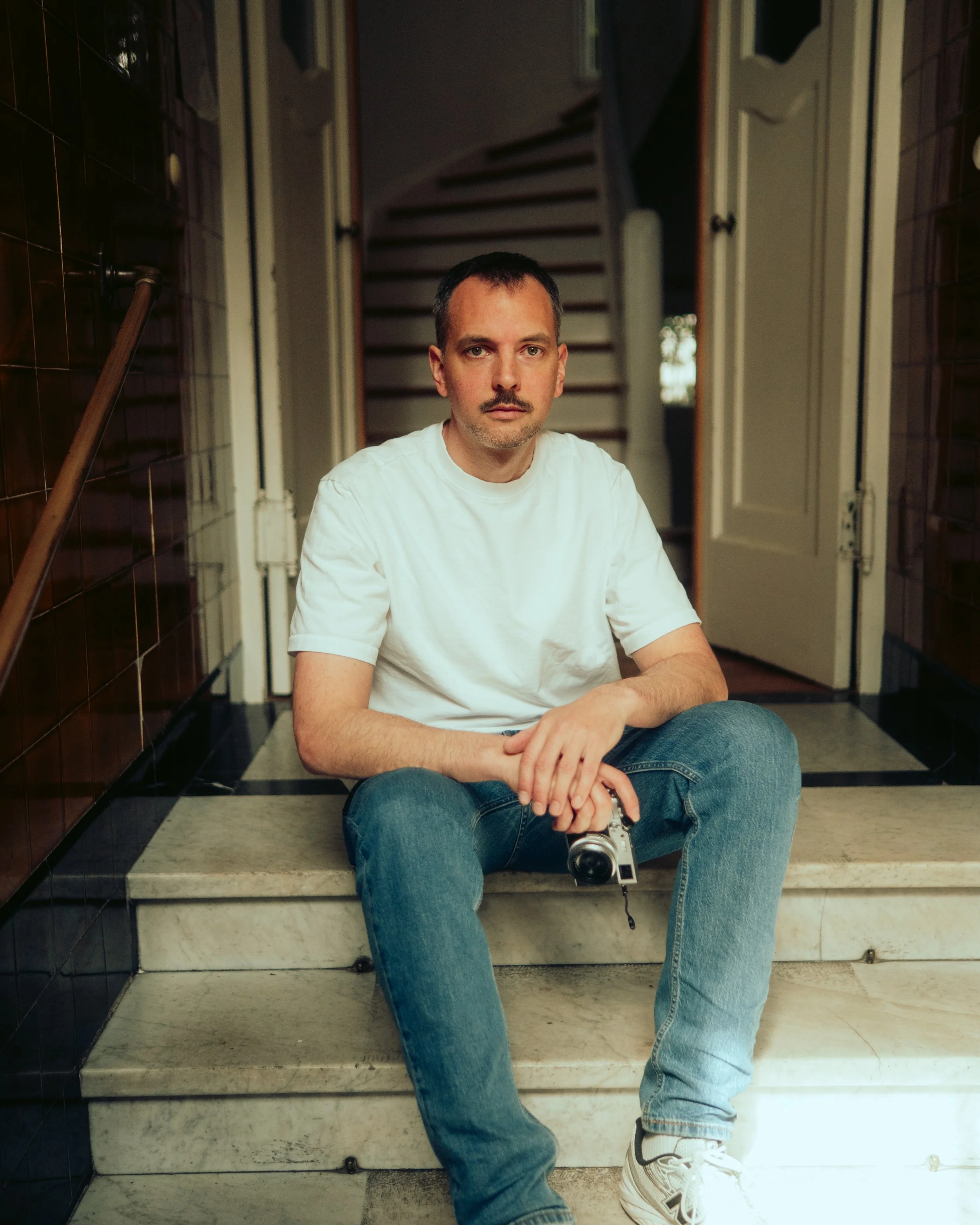 Fotograf Julian Scherrmann aus dem Saarland sitzt in Saarbrücken mit einer Kamera in der Hand auf einer Treppe.