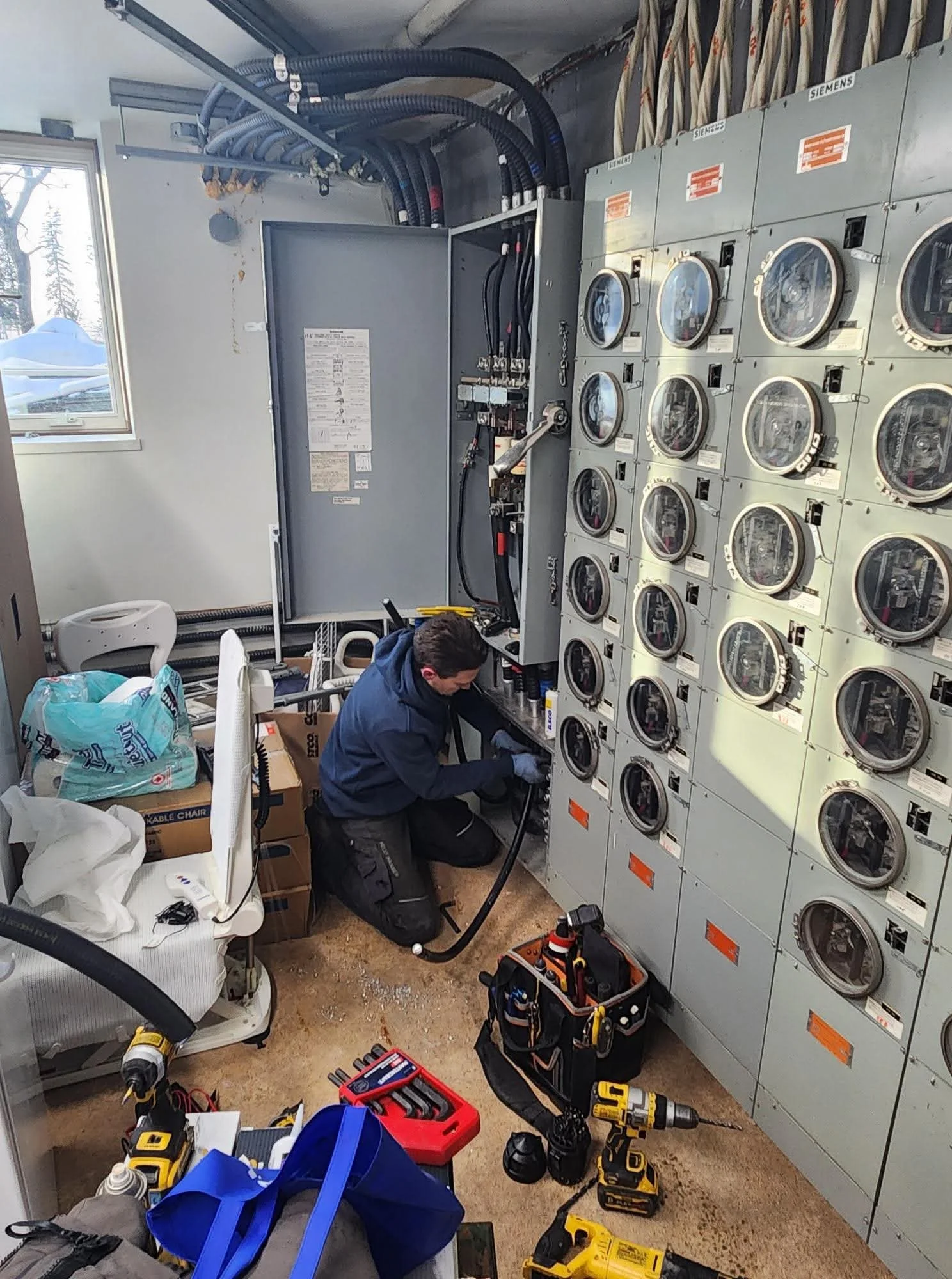 A maintenance worker repairs electrical equipment in a laundry room filled with washing machines and laundry supplies.