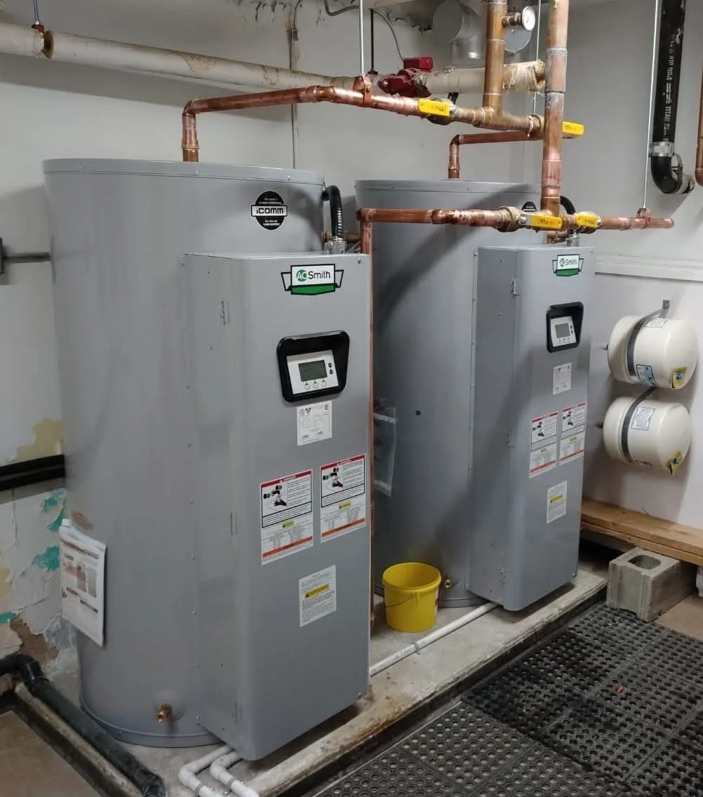 Two water heaters with digital controllers, copper piping, and yellow valves in a utility room.