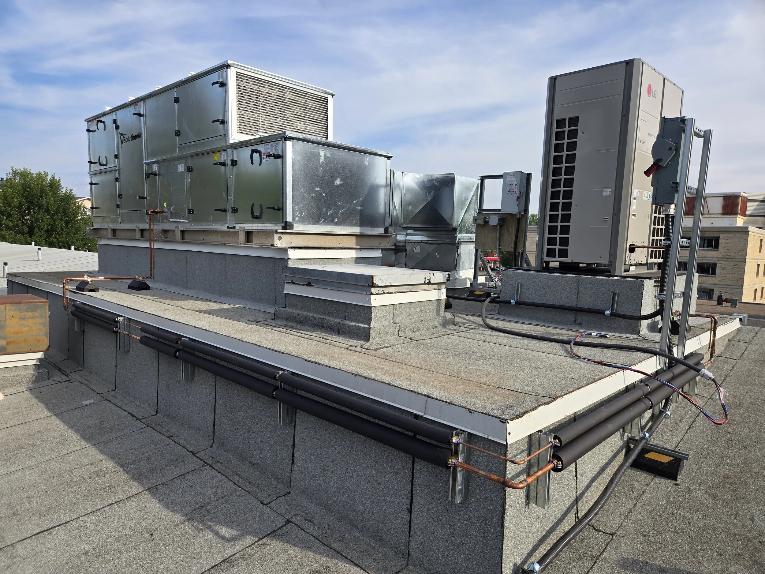 Rooftop HVAC units and air conditioning equipment installed on a building's flat roof, with blue sky and some clouds above.